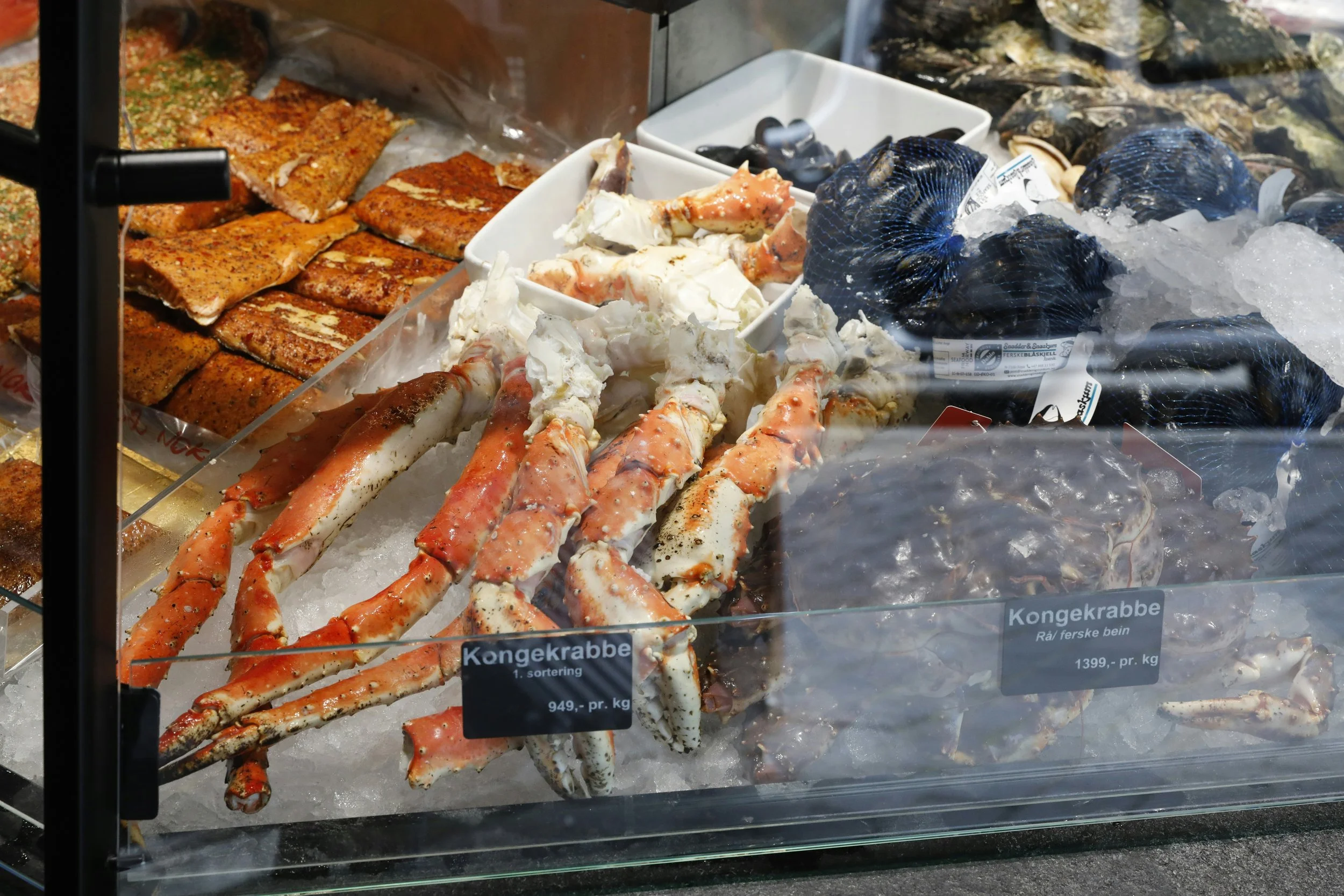 Fresh king crab legs and fillets displayed on ice inside a seafood market, with signs indicating prices per kilogram.