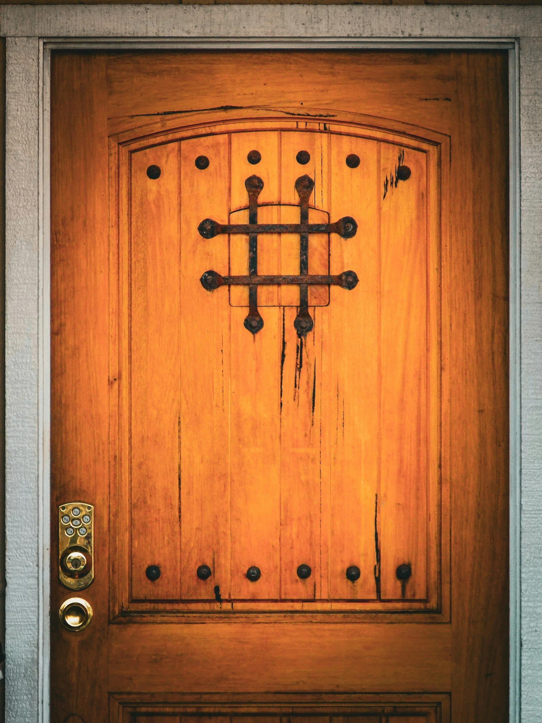 A wooden front door with black metal hinges and decorative nails, and a side panel with a keyhole and deadbolt lock.