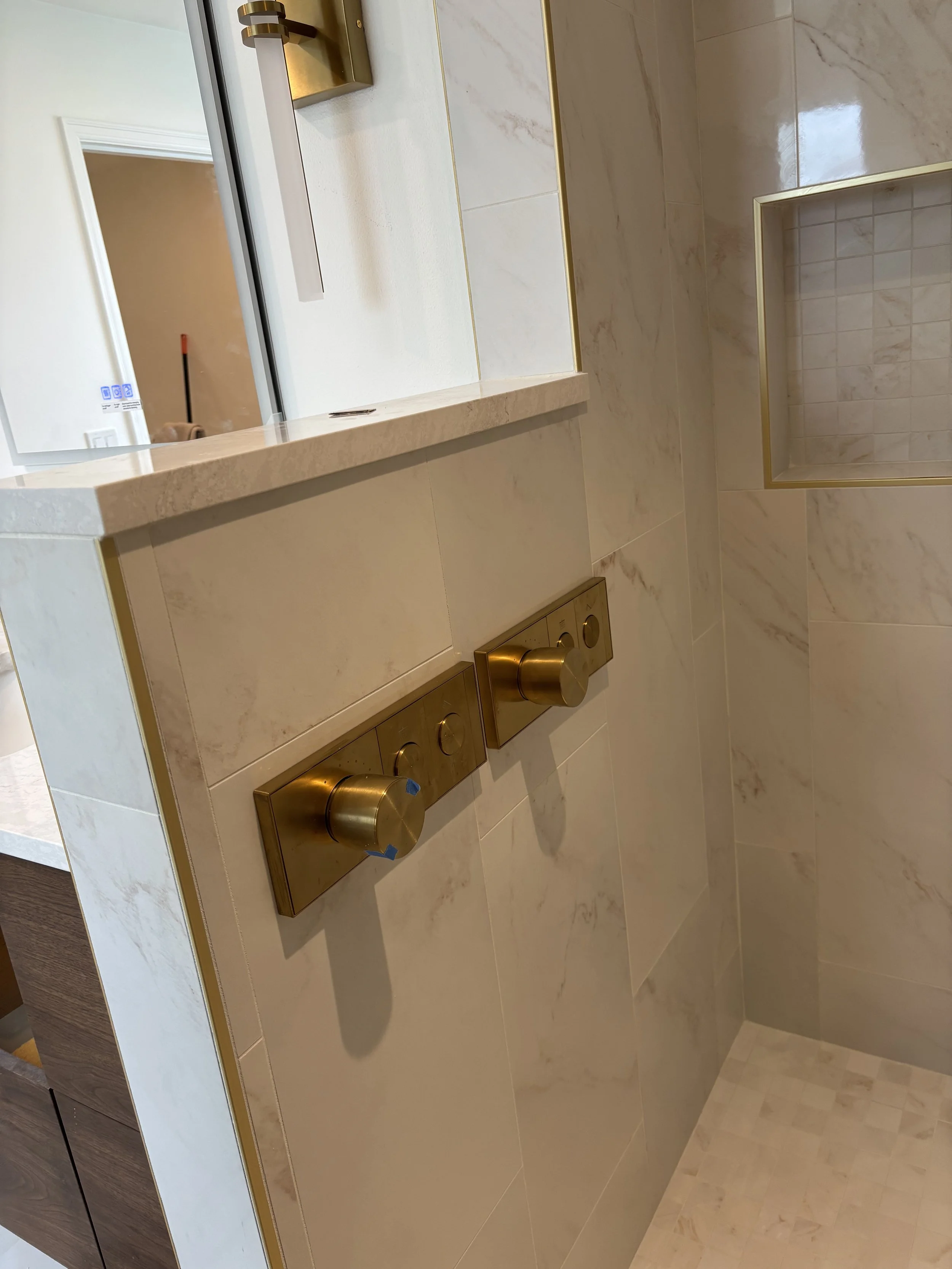 Close-up of a marble bathroom wall with gold trim and a built-in shower niche.