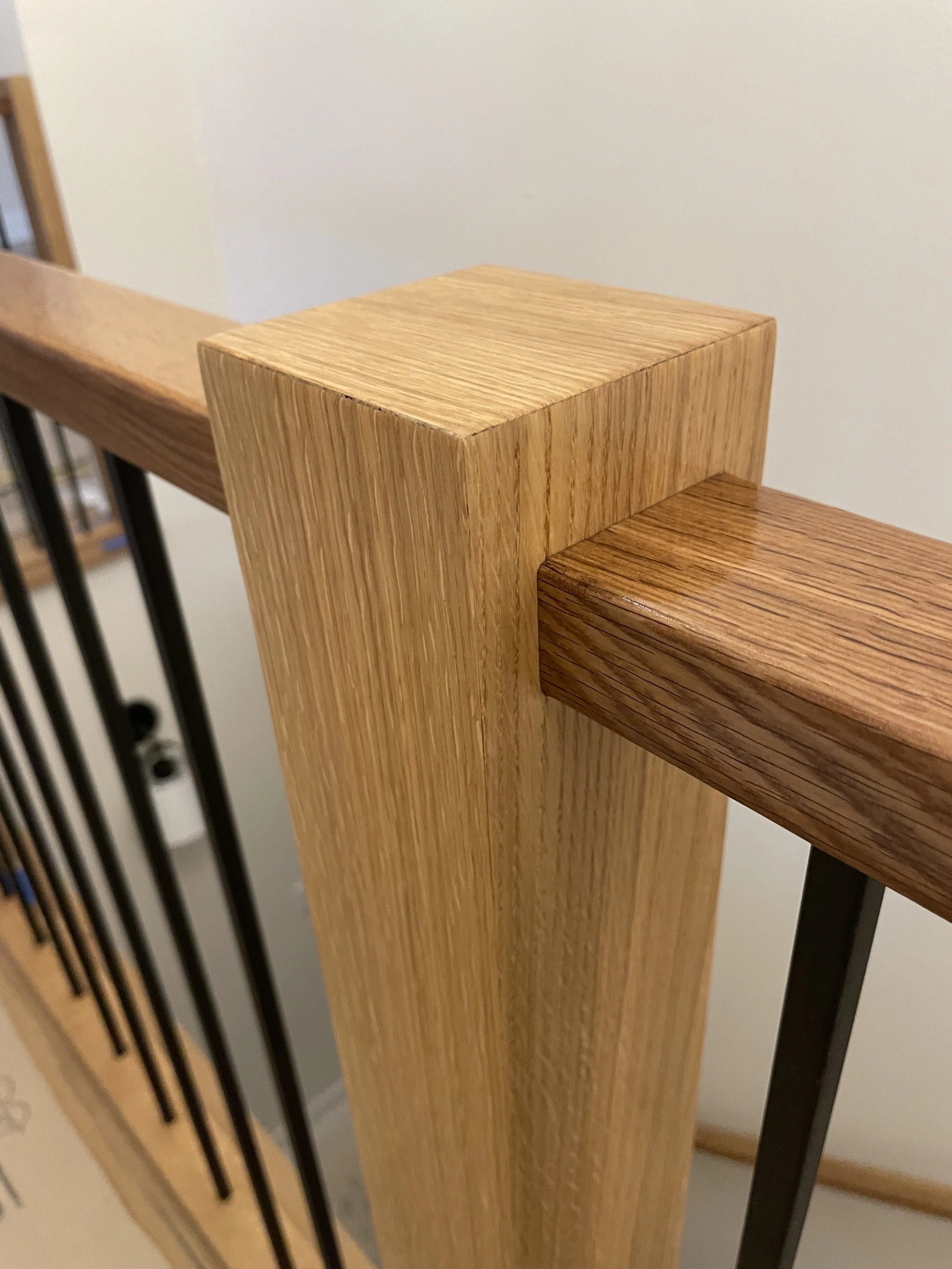 Close-up of a wooden handrail on a staircase with black vertical balusters.
