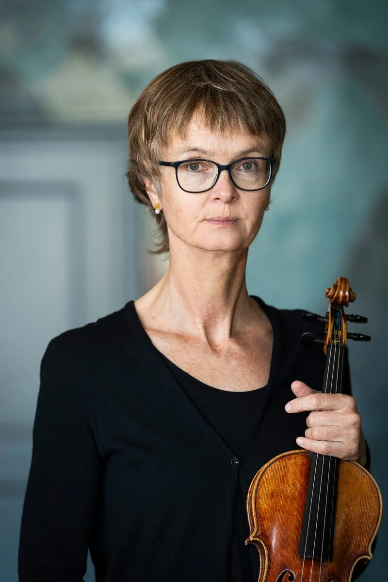 A woman wearing glasses and a black top holding a violin.