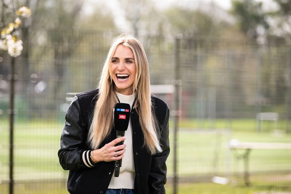 Lächelnde blonde Reporterin mit RTL-n-tv-Mikrofon in einem Park