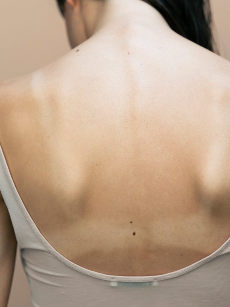 Nahaufnahme des oberen Rückens einer Person mit sichtbaren Schulterblättern und kleinen Muttermalen