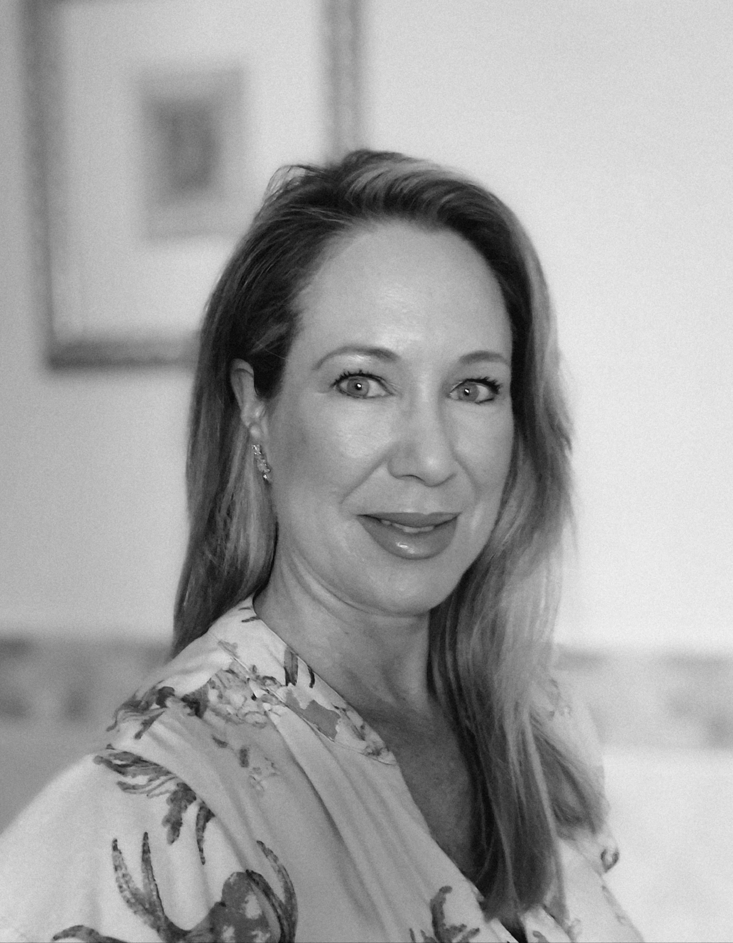 Black and white photograph of a smiling woman with long hair, wearing earrings, and a top with a dragonfly pattern.