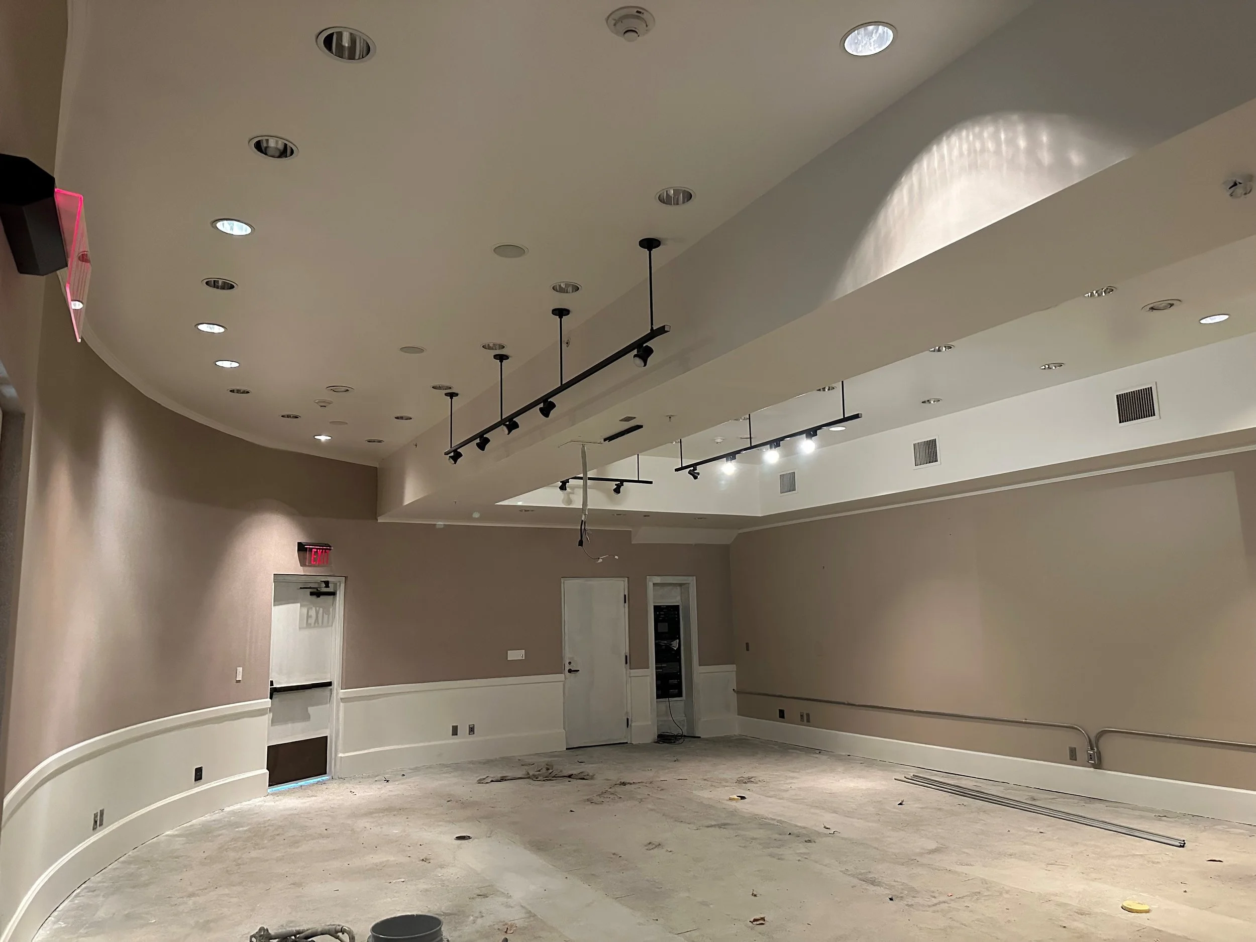 Interior of a room under construction with a curved wall, a ceiling with recessed lighting, and some construction materials on the floor.