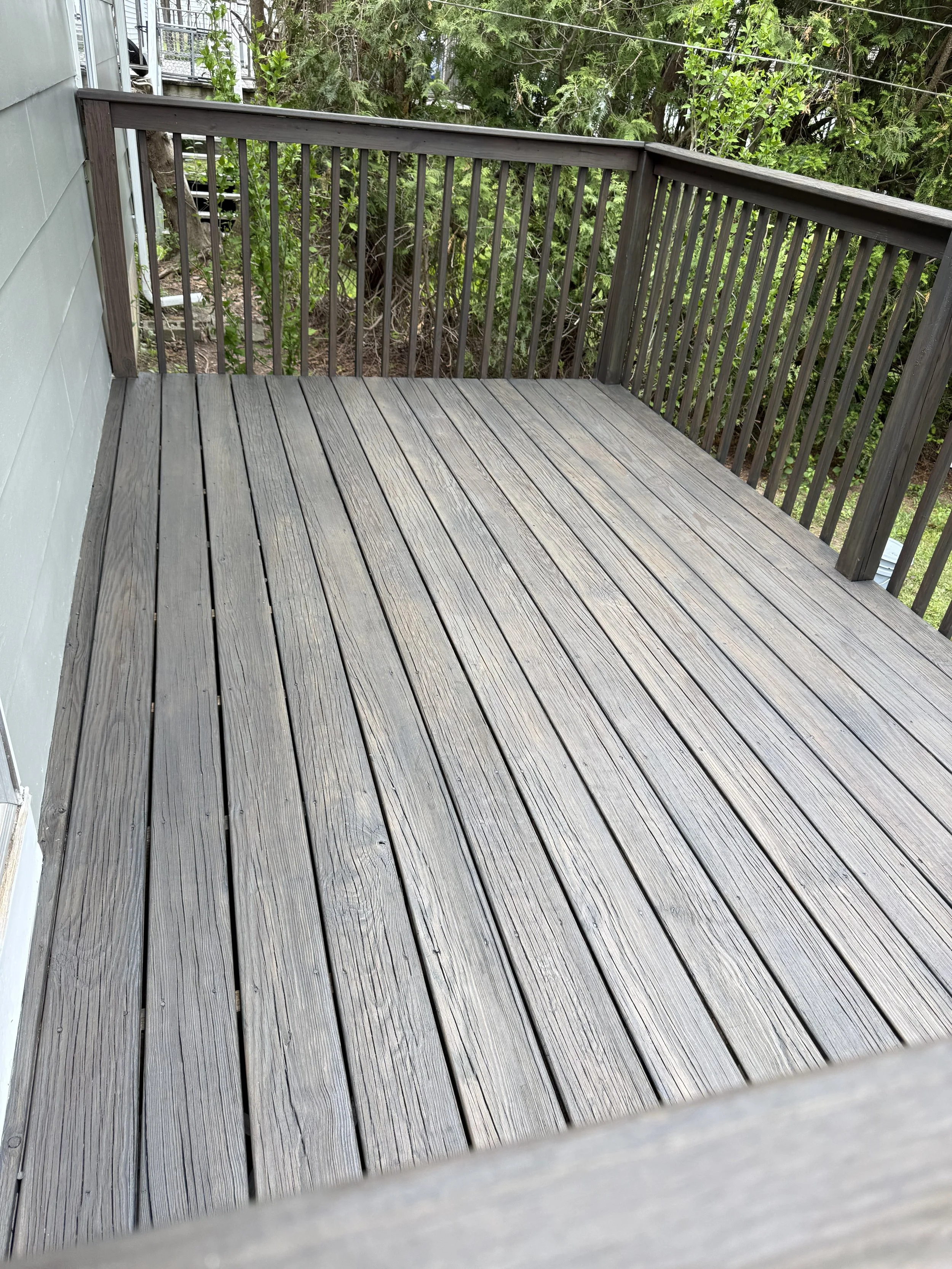 A wooden deck with horizontal planks and a railing, overlooking greenery and trees.