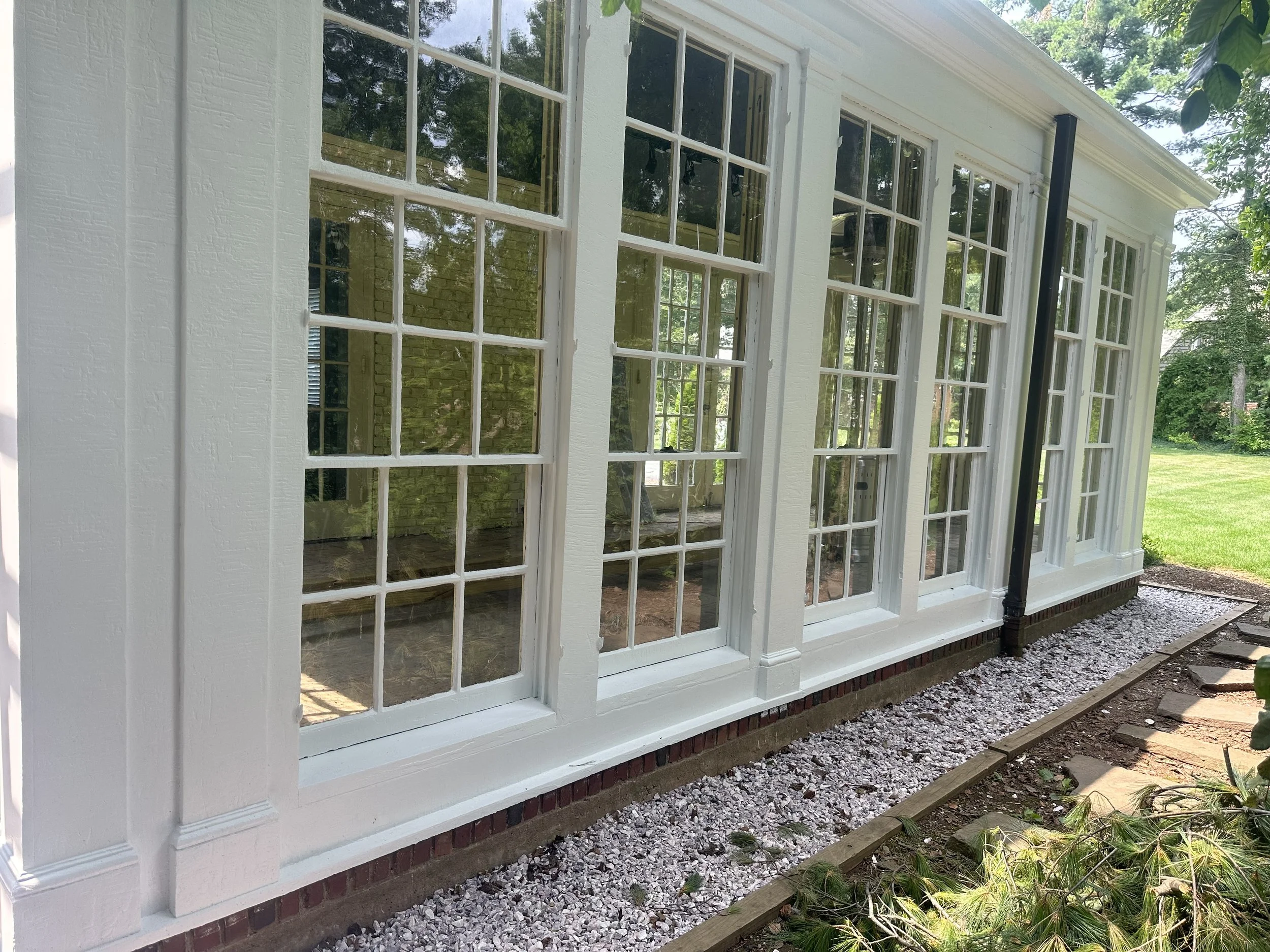 Close-up of a white building with large multi-pane windows, surrounded by greenery, on a sunny day.
