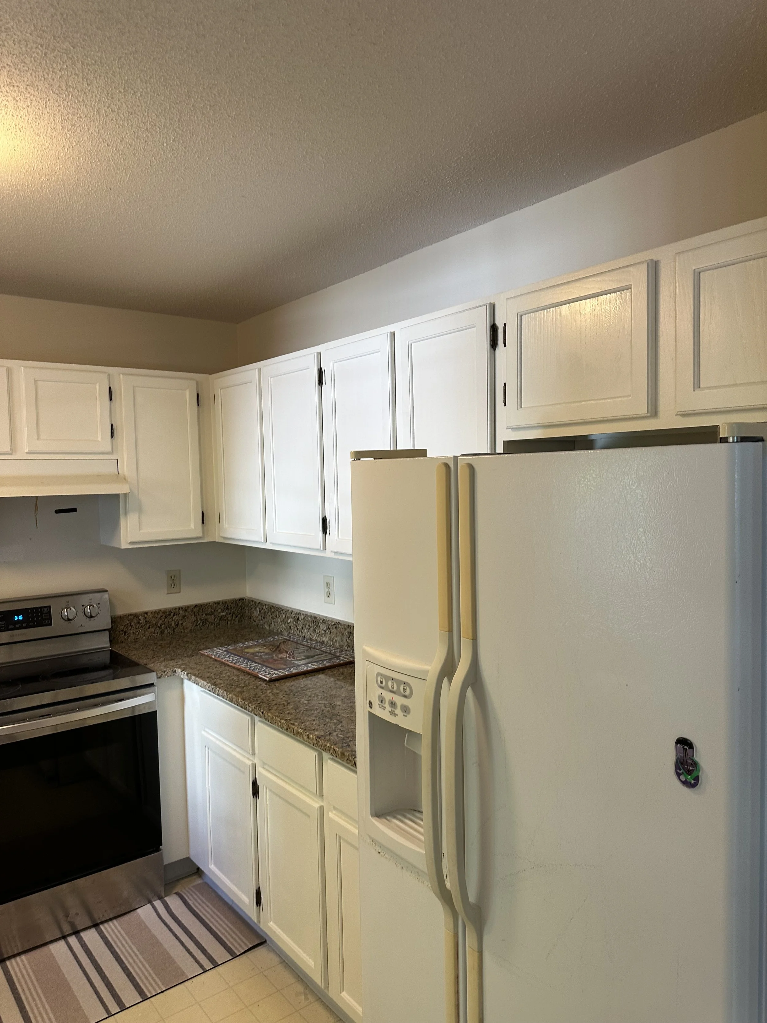 Kitchen with white cabinets, a black stove, a granite countertop, a white refrigerator, and a striped rug on a tan tile floor.