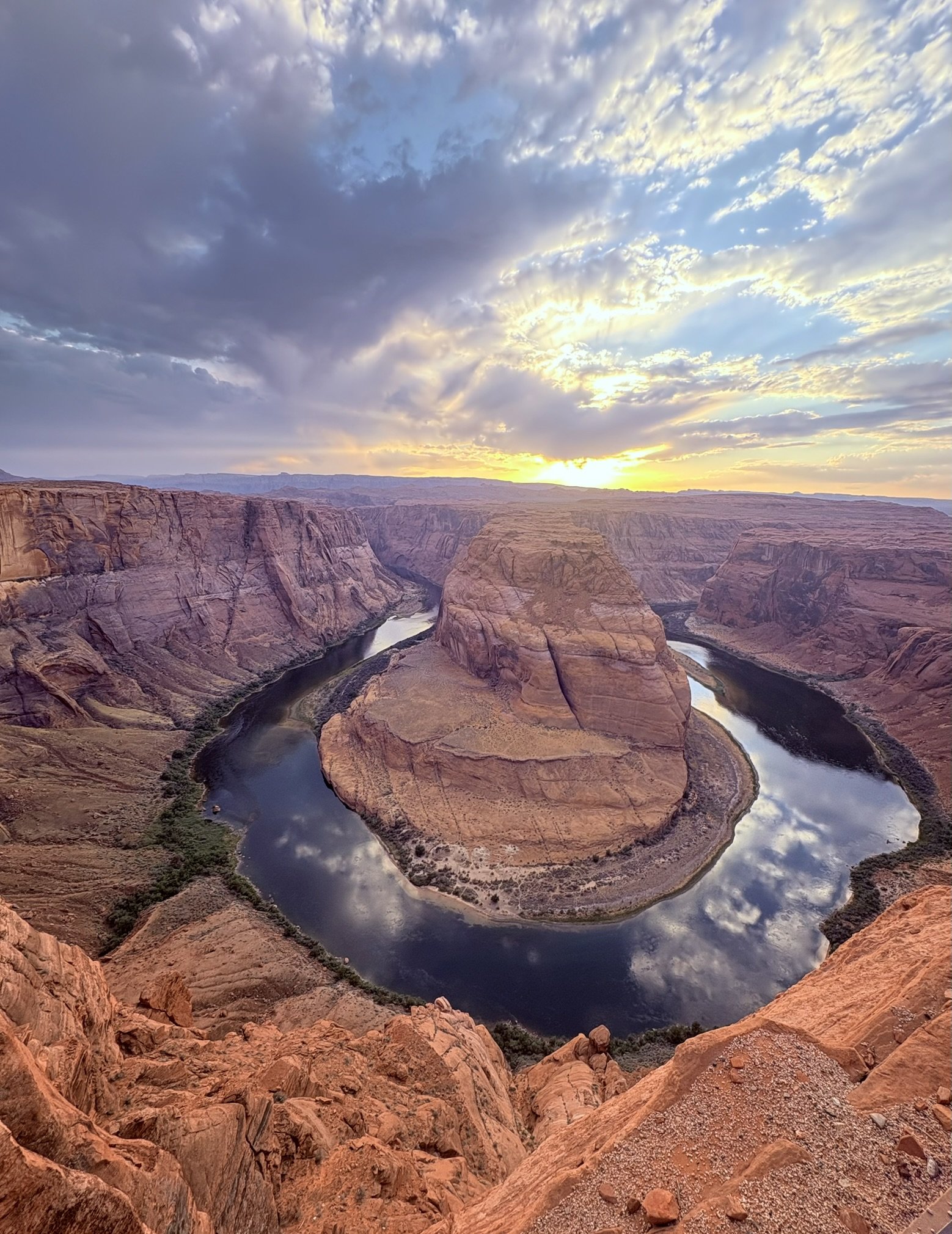Canyon avec un fleuve serpentant au fond, ciel avec nuages illuminés par le soleil couchant.