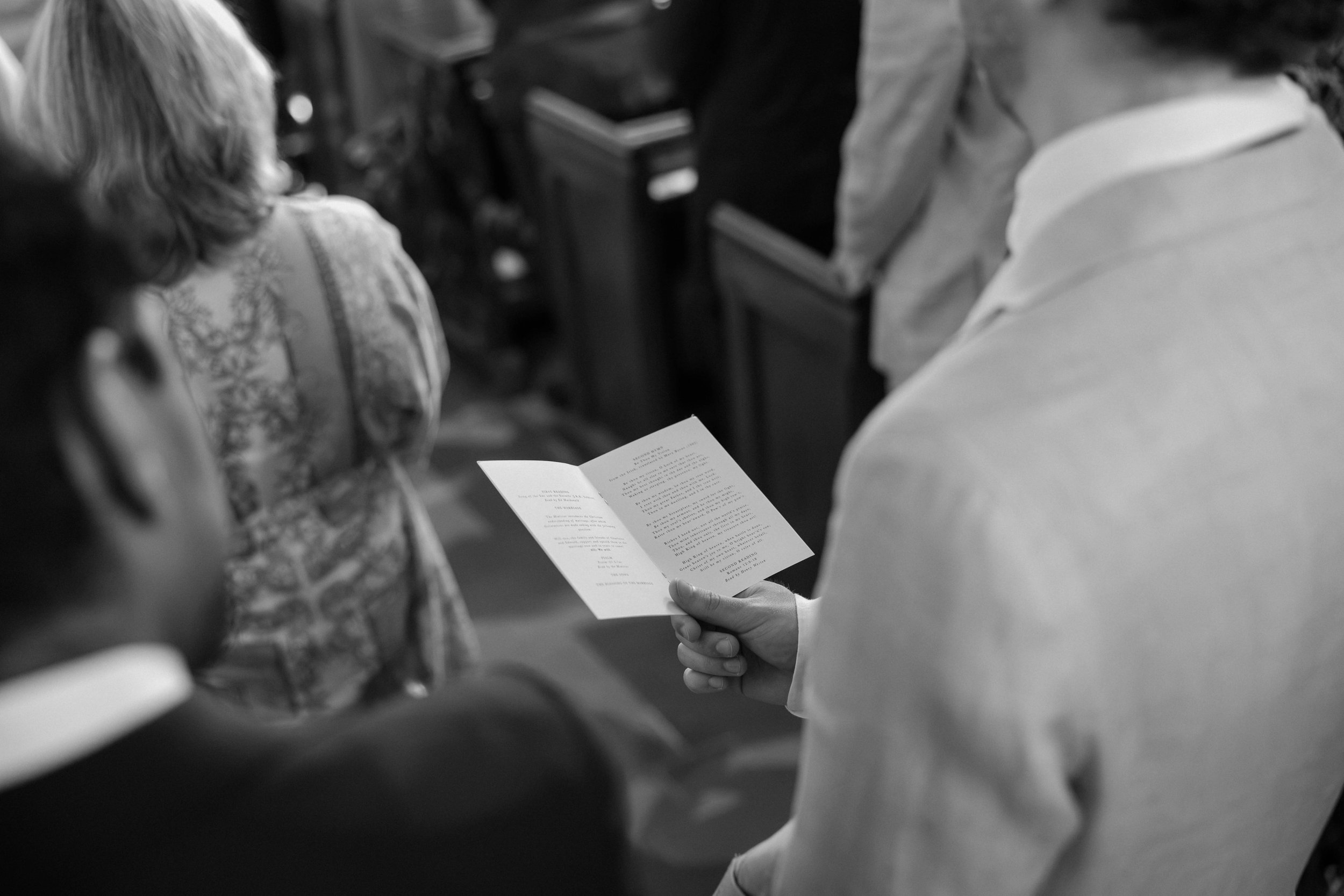 A person holding and reading a small printed program or booklet during a formal event, with other attendees around.