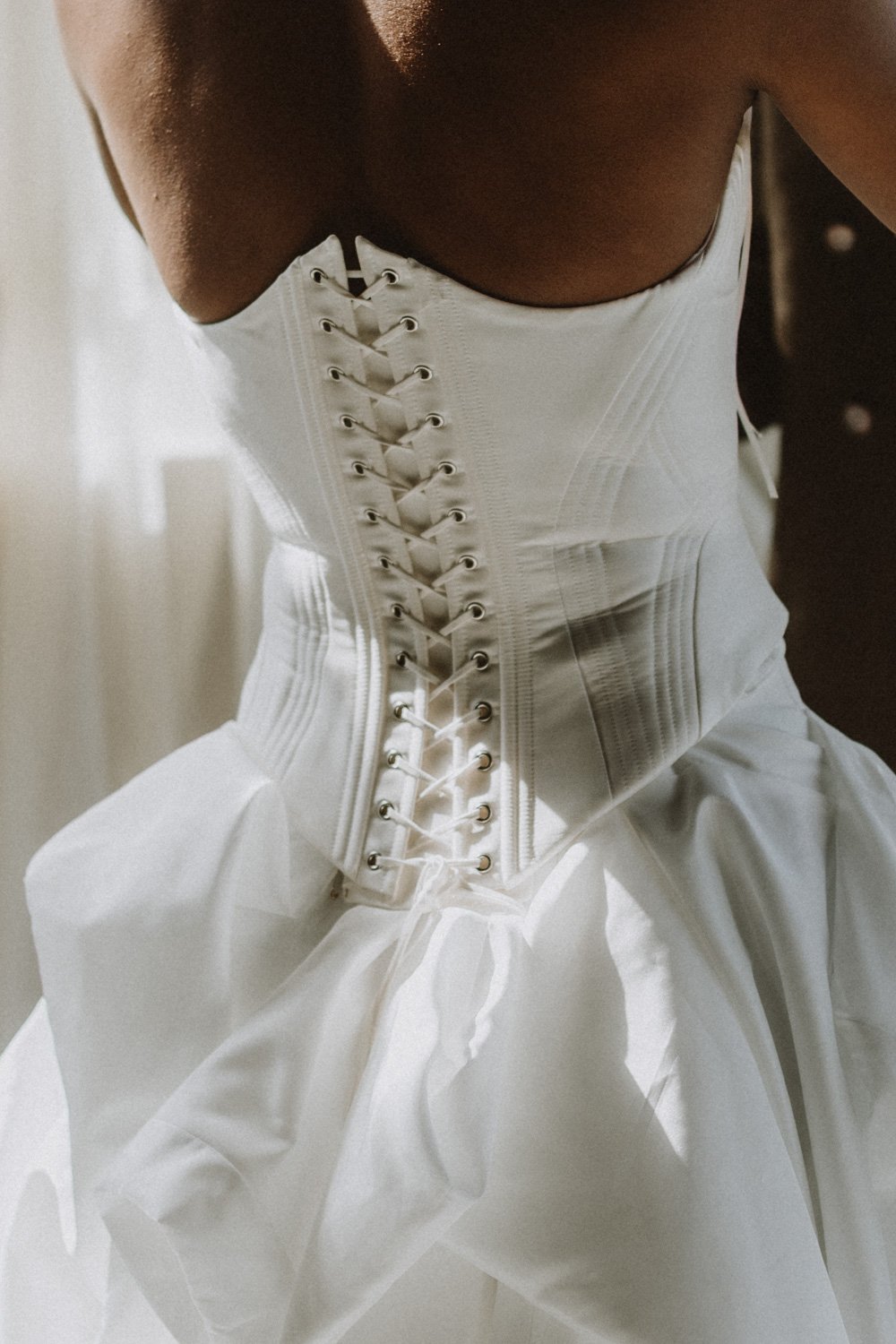 A person wearing a white corset-style garment with lacing in the front, made of shiny fabric, paired with a flowing white skirt or dress.