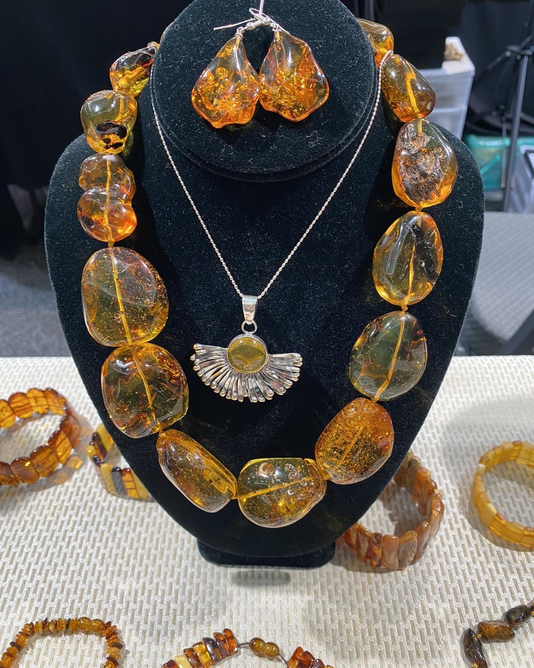 Jewelry display featuring amber-colored necklace, earrings, and bracelets on a black velvet bust and a white fabric table.
