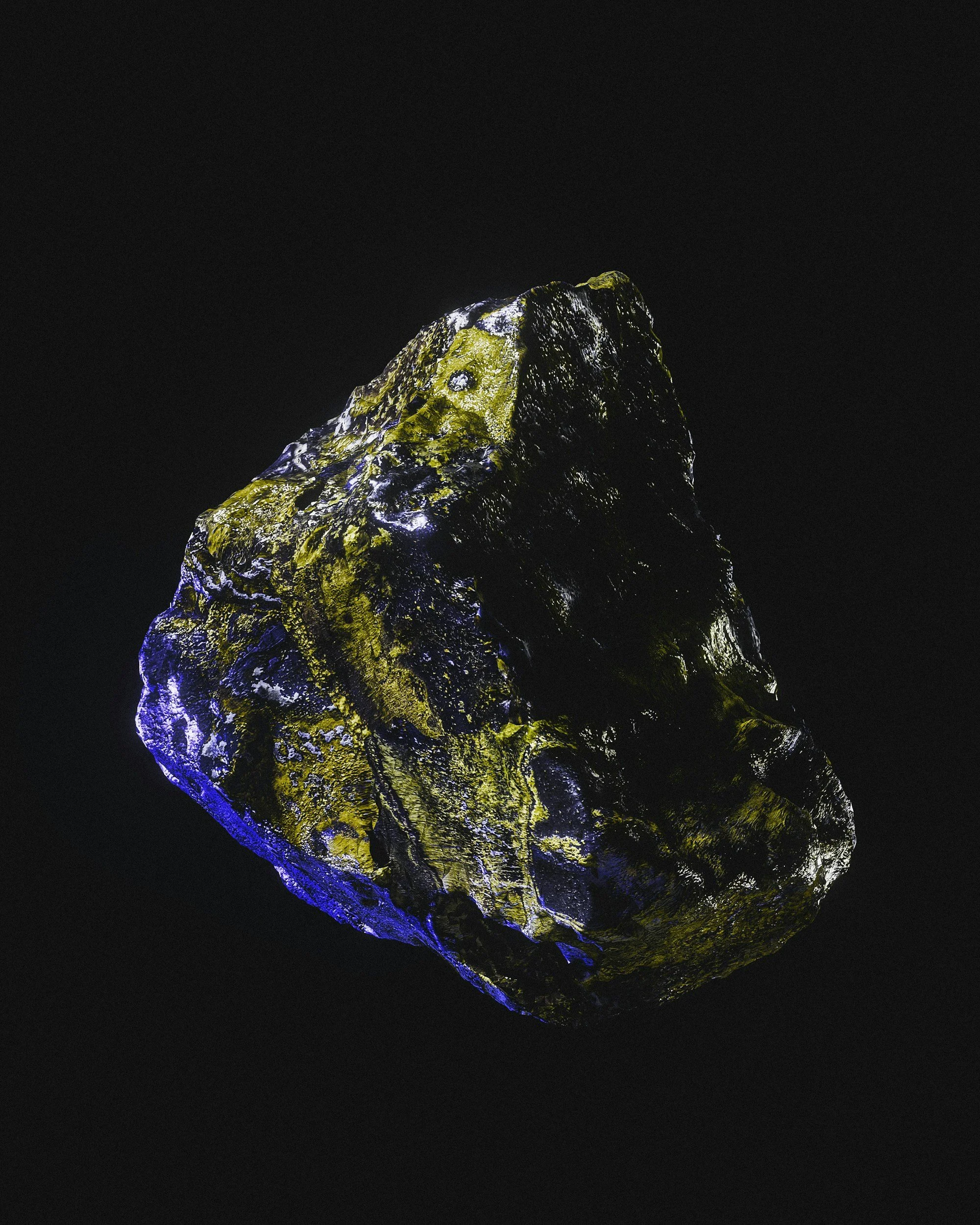A dark rock with patches of yellow and white light reflects against a black background.