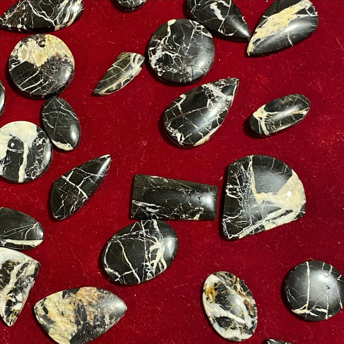 A collection of black and white marbled stones of various shapes and sizes placed on a red surface.
