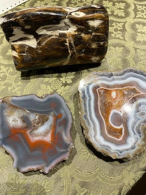 Three polished stones with banded patterns in shades of brown, gray, and white, placed on a green patterned fabric surface.