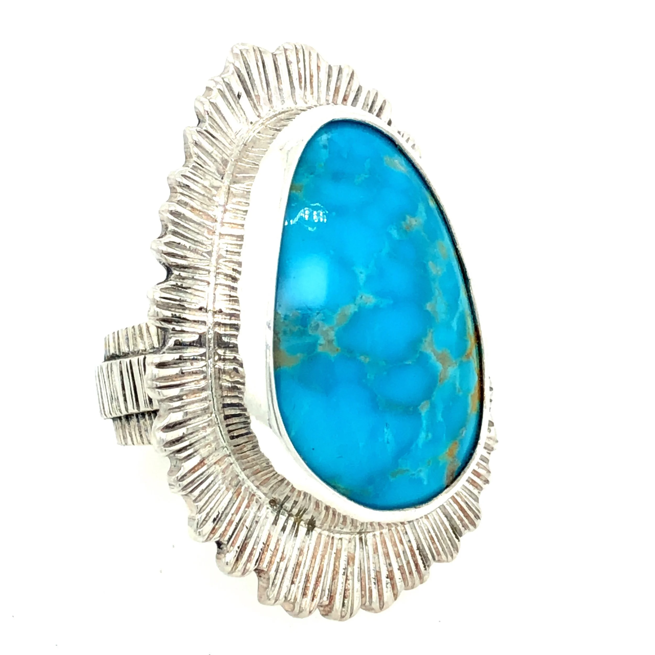 A turquoise oval-shaped gemstone with brown and gold veins, set in a silver pendant with a decorative border of radiating lines.