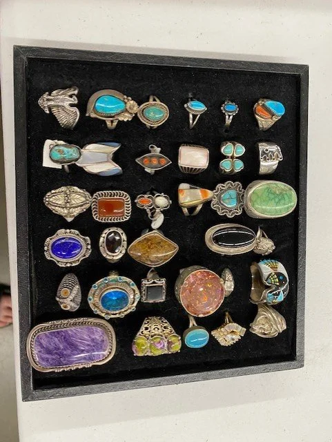 Collection of 31 jewelry rings and brooches in a black display box.