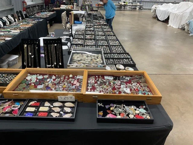 Display of various jewelry items, including rings, necklaces, and brooches, arranged in trays at a marketplace or sale event.