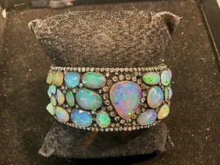 Jewelry bracelet with multicolored opal-like stones and a large central iridescent stone, set on a gray surface.