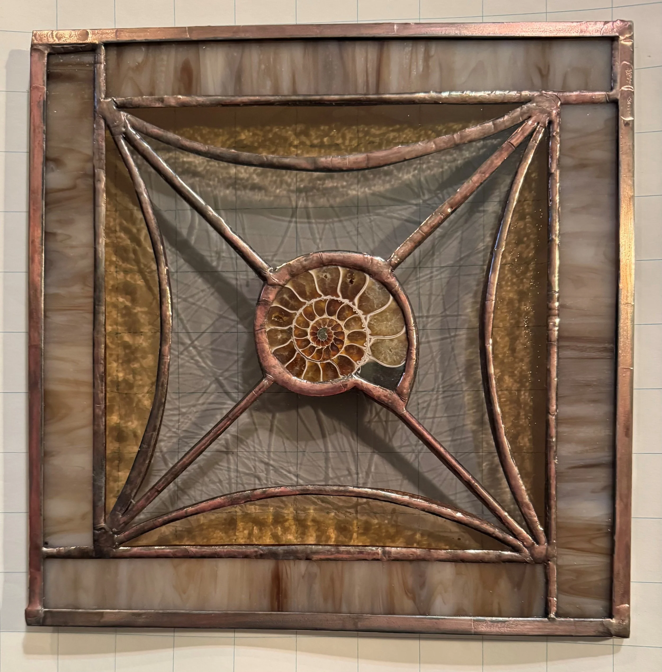 This is a large framed artwork or sculpture resembling a nautilus shell, crafted from copper pipes and metal rods, with an intricate spiral design.