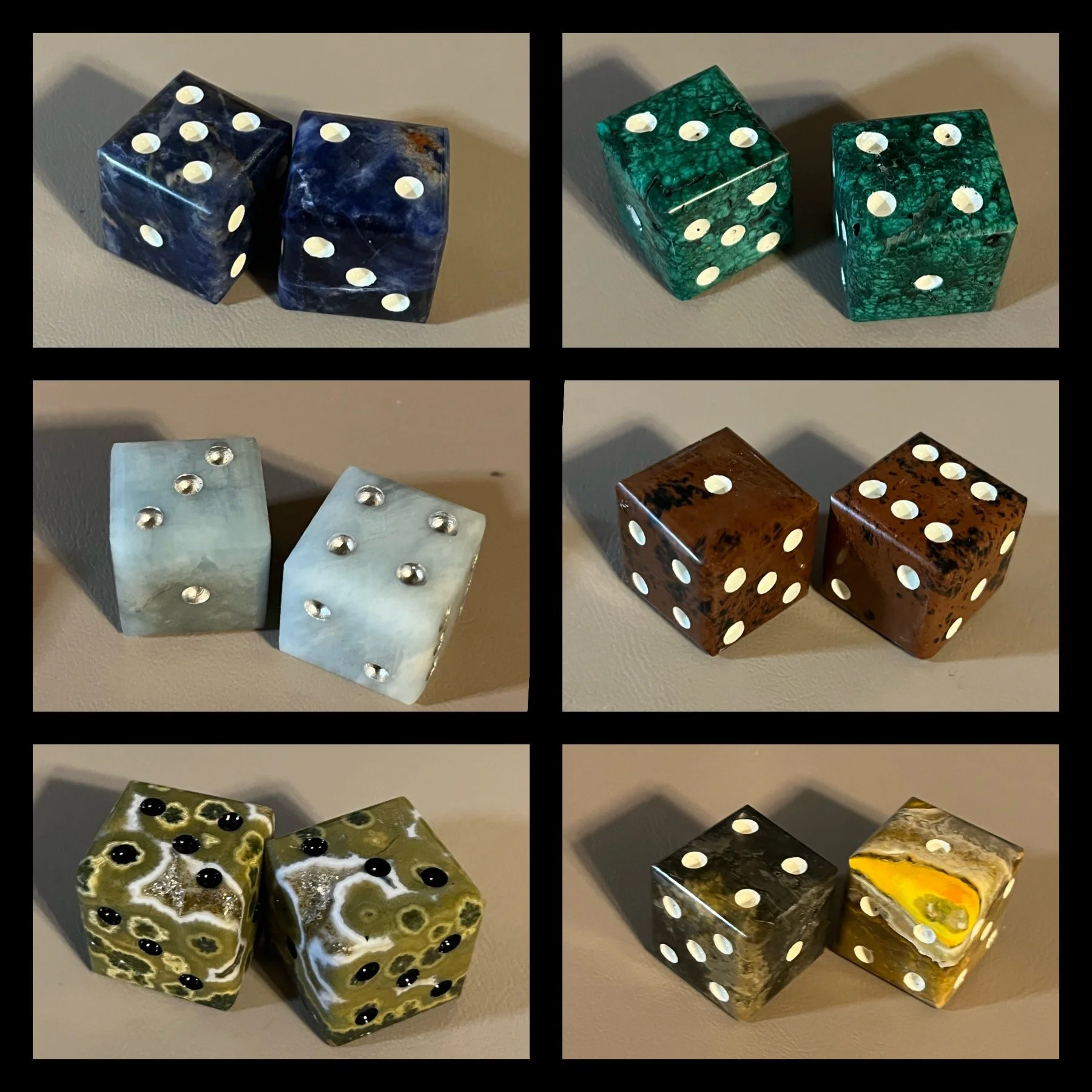 Four sets of decorative dice with various marbled colors and patterns, including dark blue, green, white, brown, and yellow, each set featuring white or black pips on their faces, arranged on a neutral-colored surface.