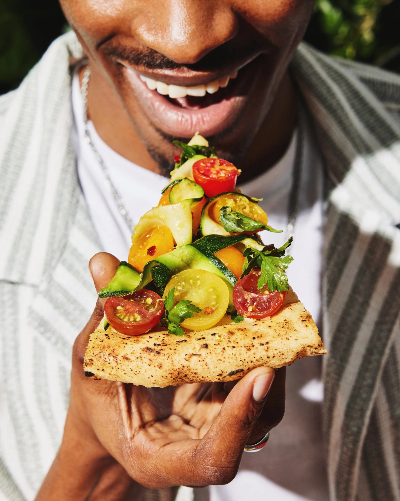 Smiling man holding a slice of vegetable-topped pizza.