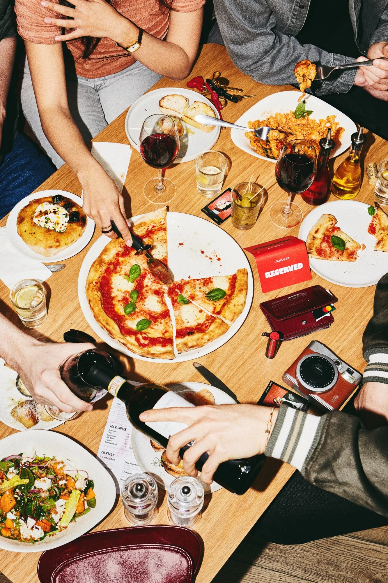 Overhead lifestyle photograph of friends sharing pizza and drinks around a restaurant table.