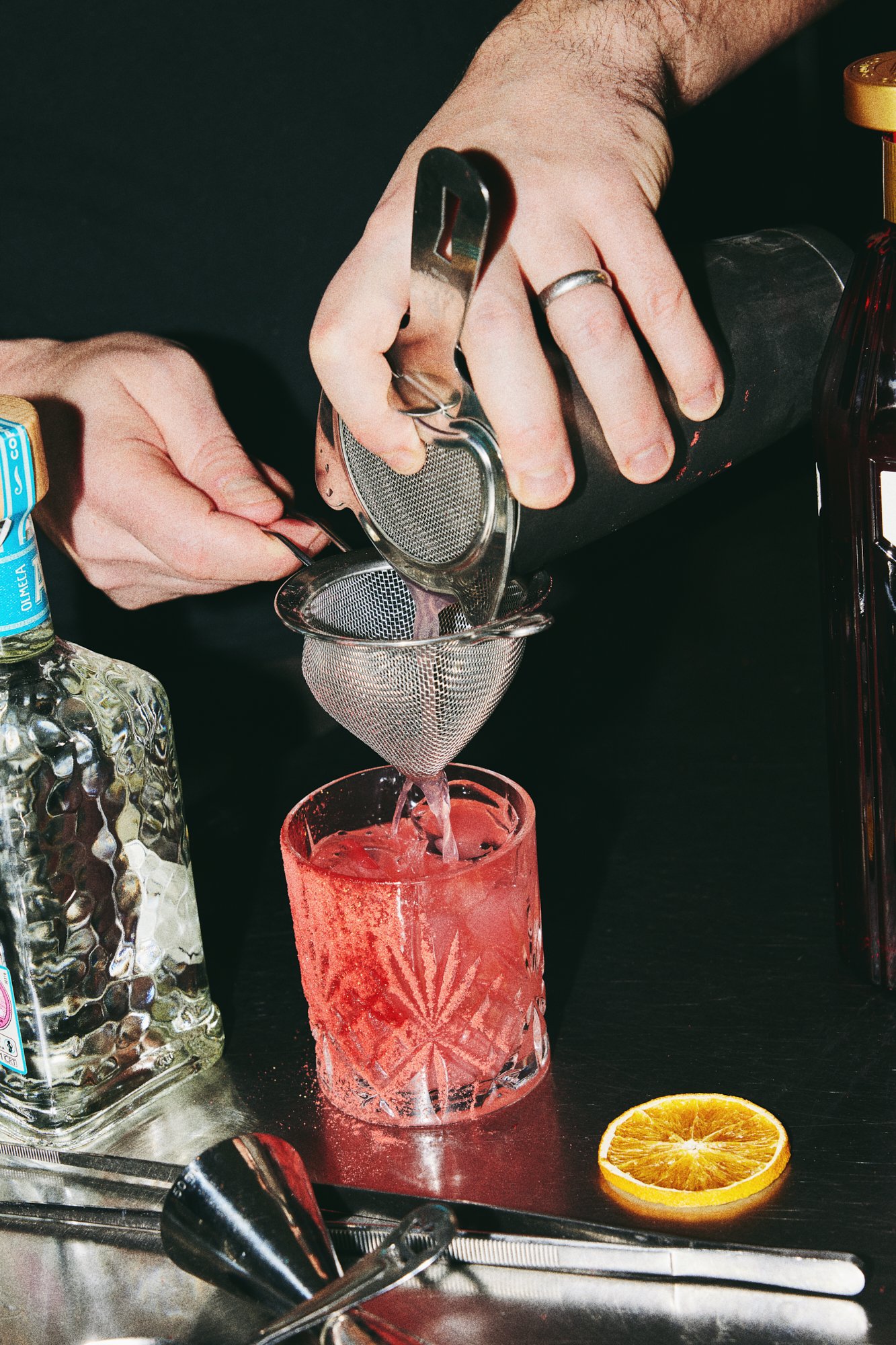Bartender straining a pink cocktail into a glass.