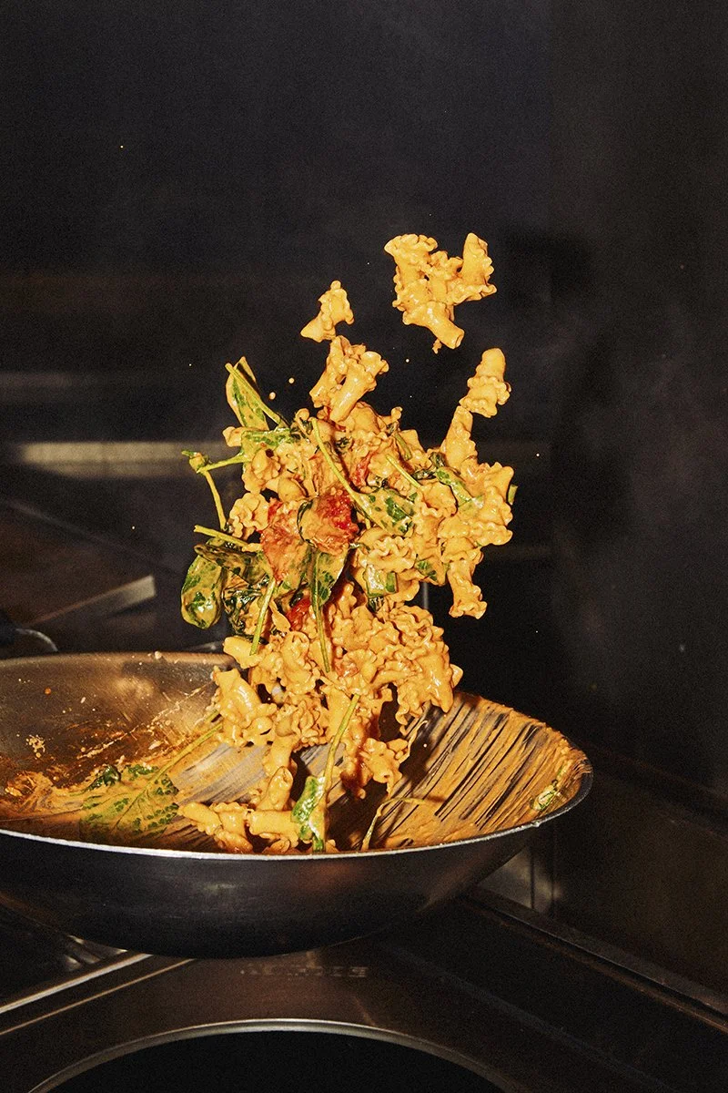 Chef tossing pasta and vegetables in a pan over a restaurant stove.