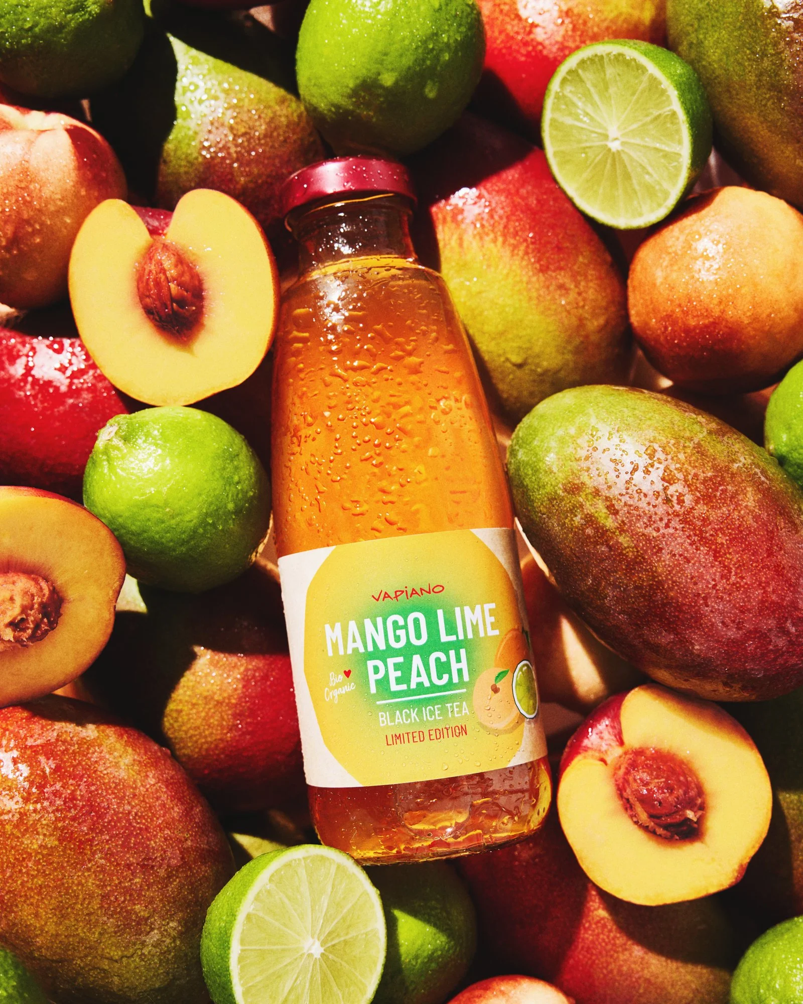 Vapiano mango, lime and peach bottled drink surrounded by fresh mangoes, peaches and limes.