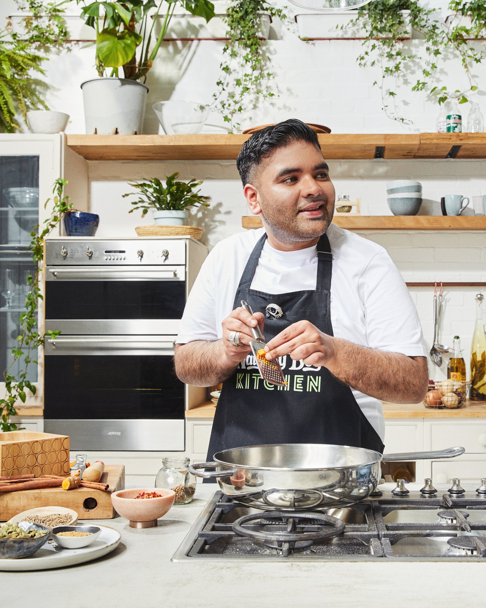 Chef standing at a kitchen hob with a frying pan and ingredients.