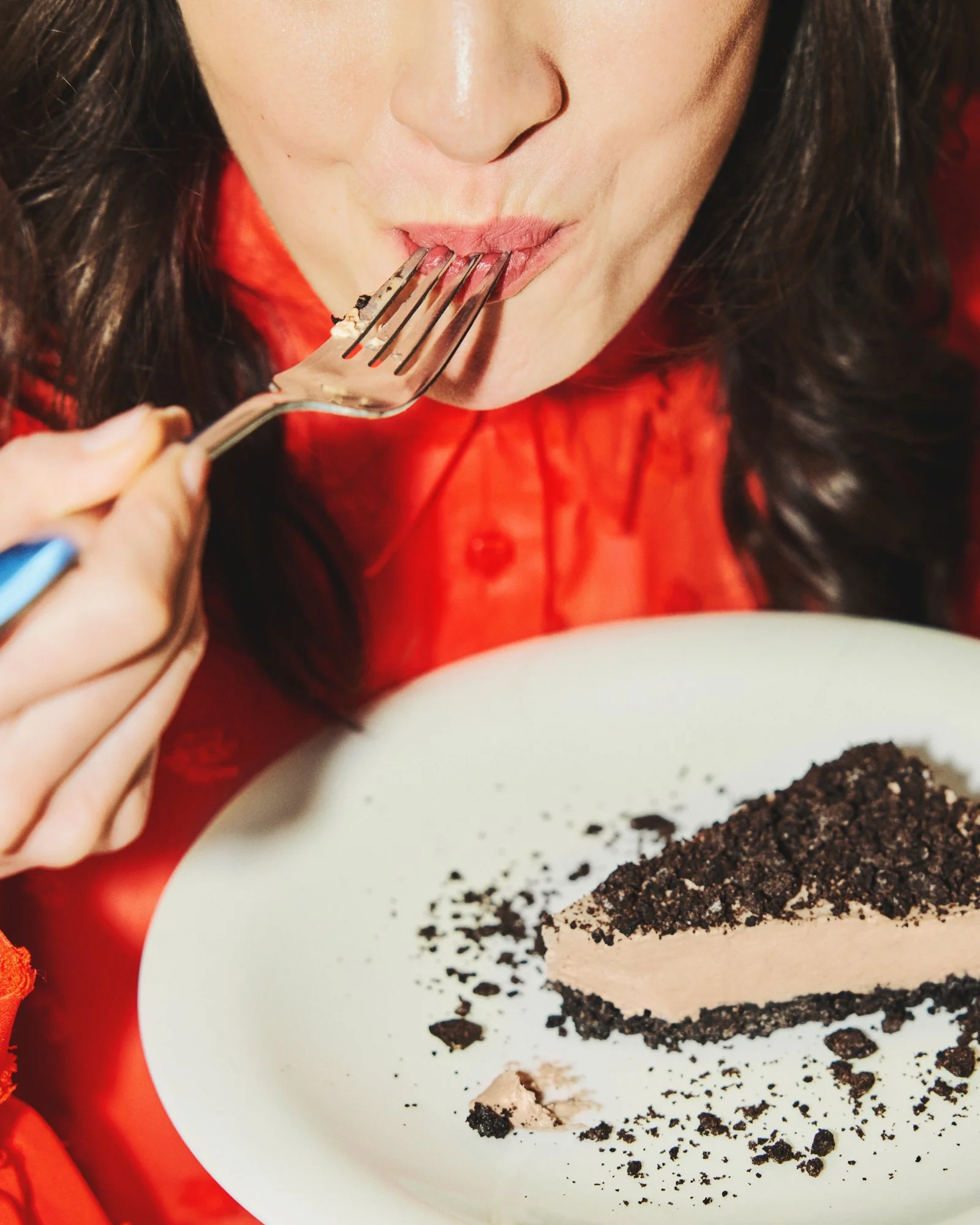 Woman in a red top enjoying a bite of a chocolate dessert.