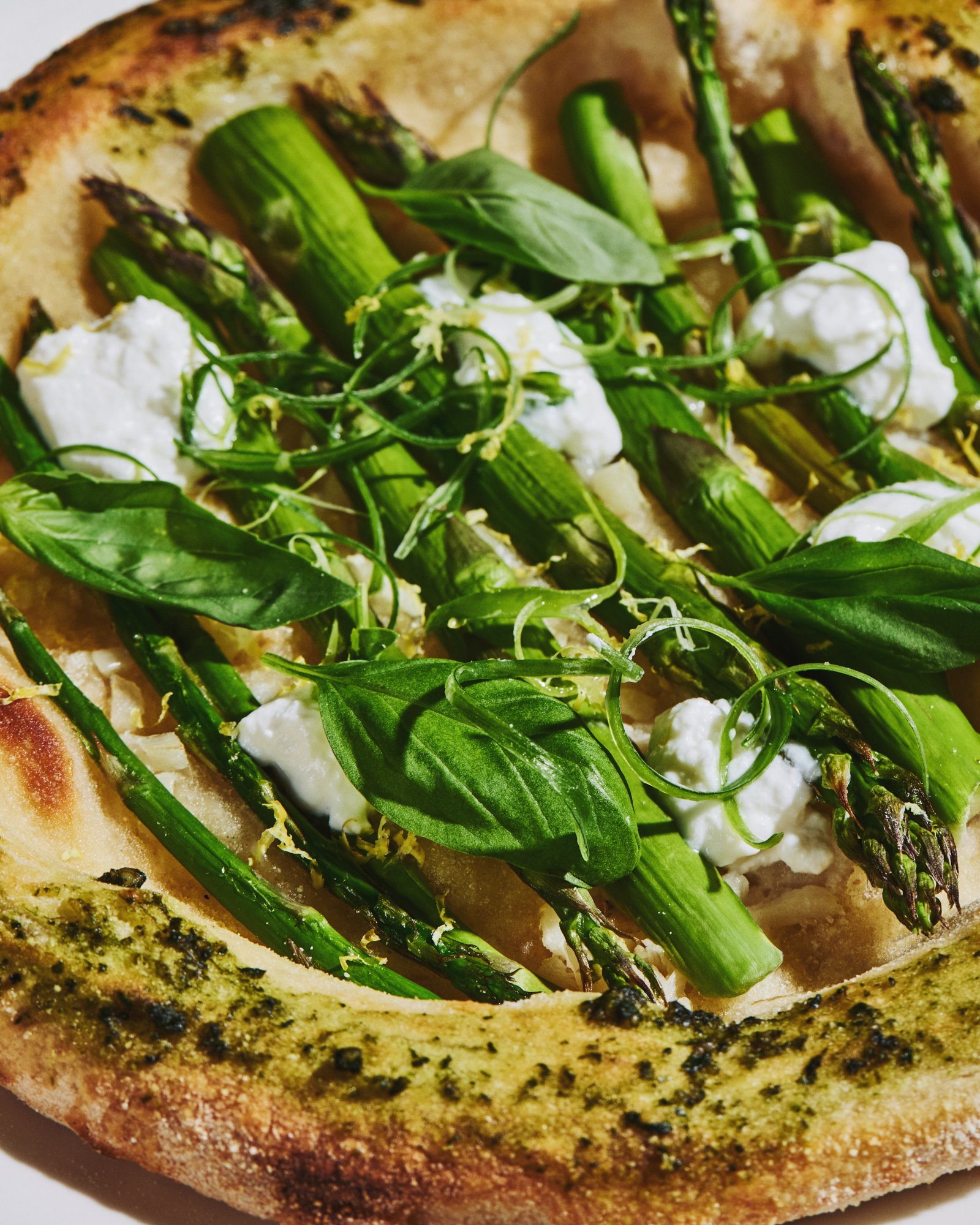 Close-up of asparagus pizza topped with green vegetables, basil and creamy cheese.