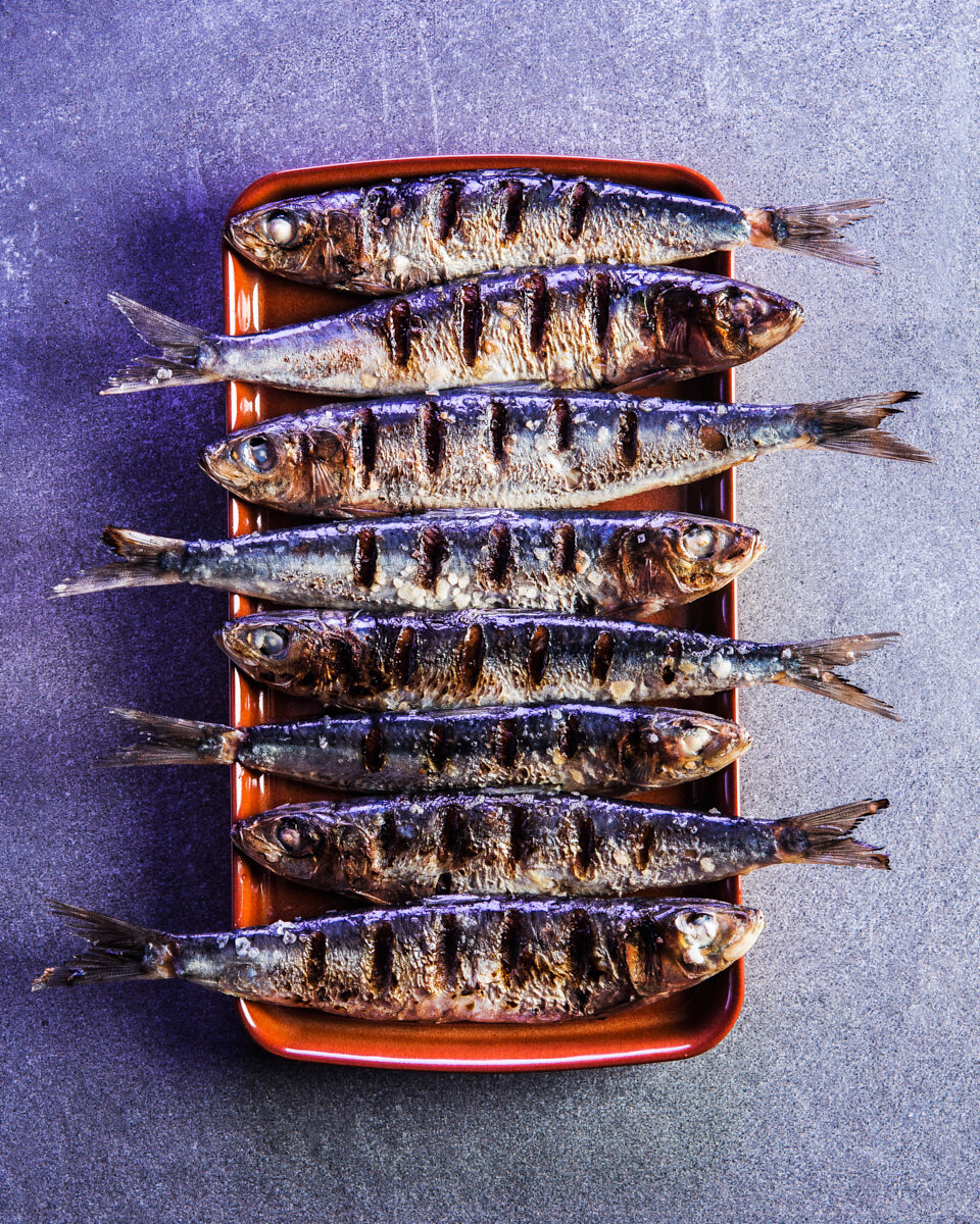 Overhead photograph of grilled whole fish arranged in a row on a ceramic tray.