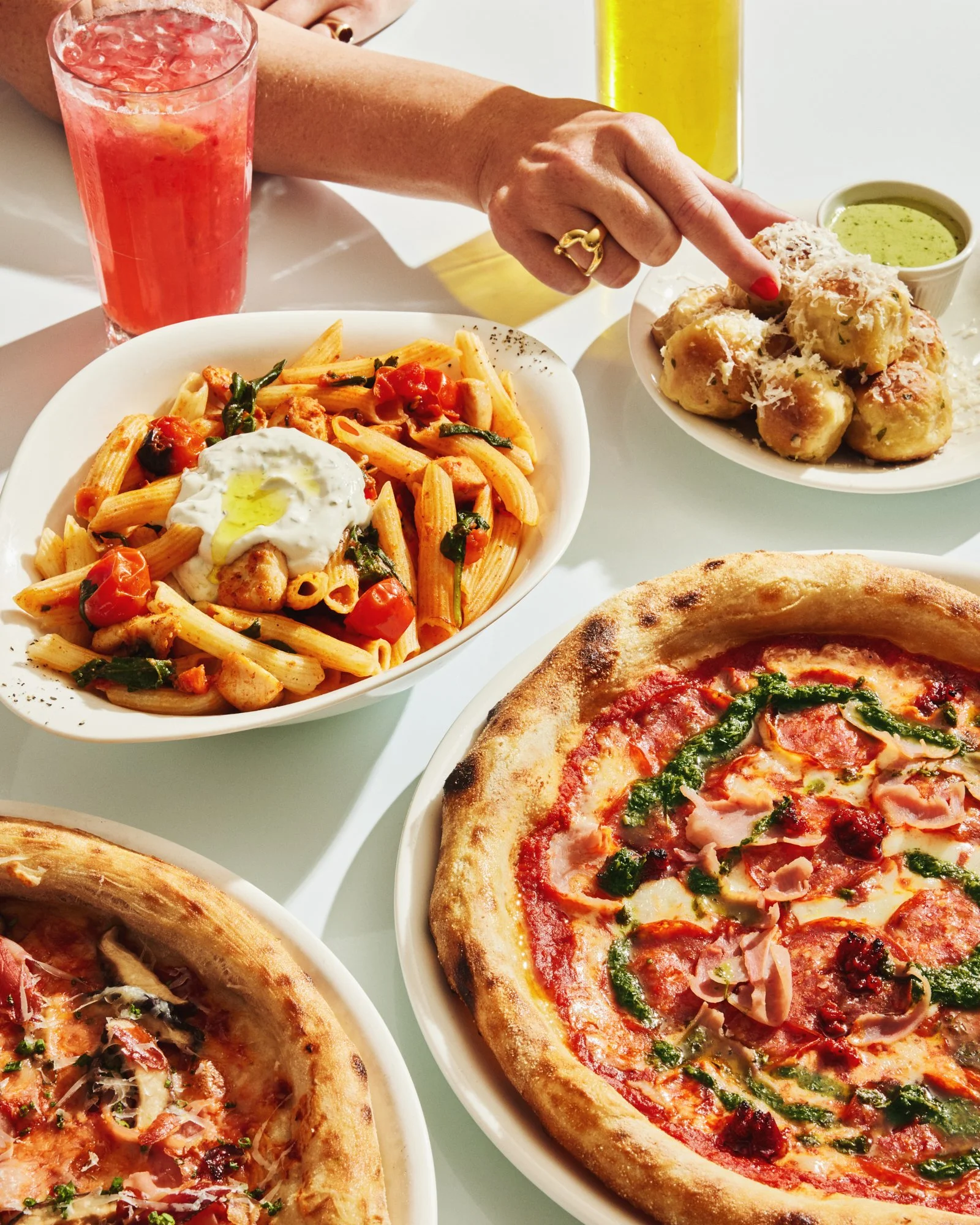 Overhead photograph of Italian pasta, pizza and side dishes being shared at a restaurant table.