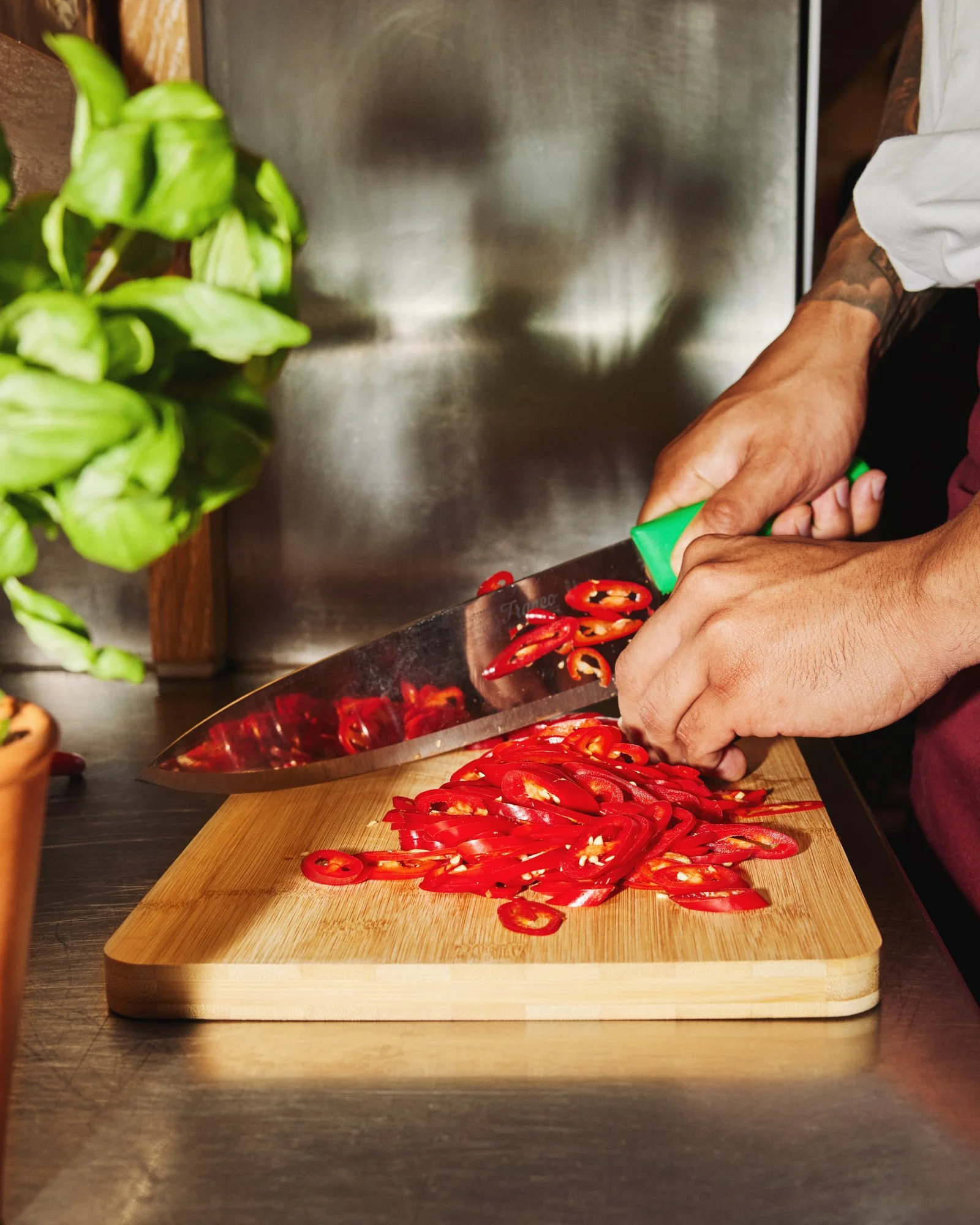 Chef slicing fresh red chillies on a wooden chopping board in a professional kitchen.