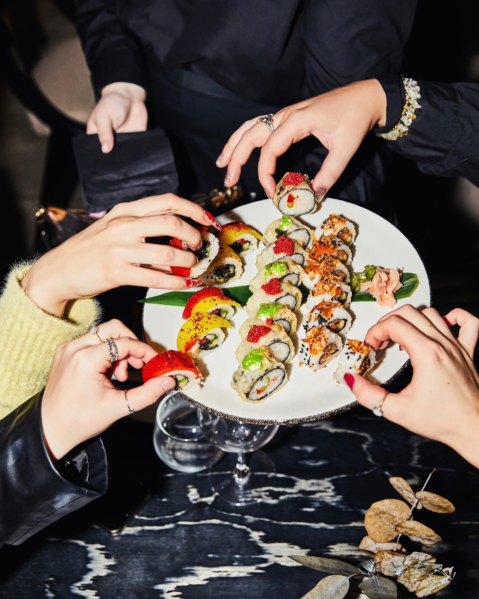 Overhead photograph of friends sharing a platter of sushi rolls.
