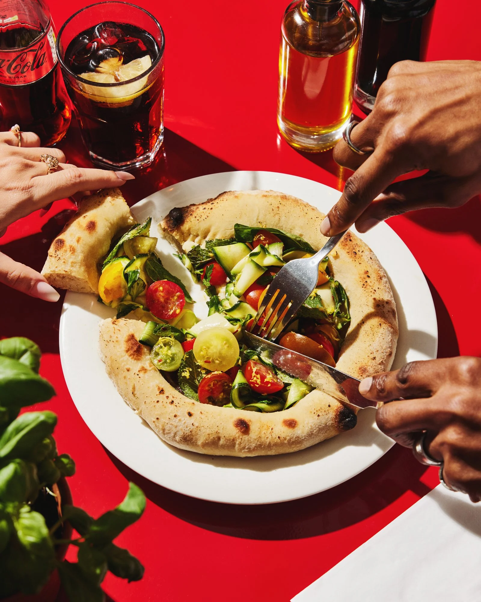 Overhead photograph of a vegetable pizza being shared by diners at a bright red table.