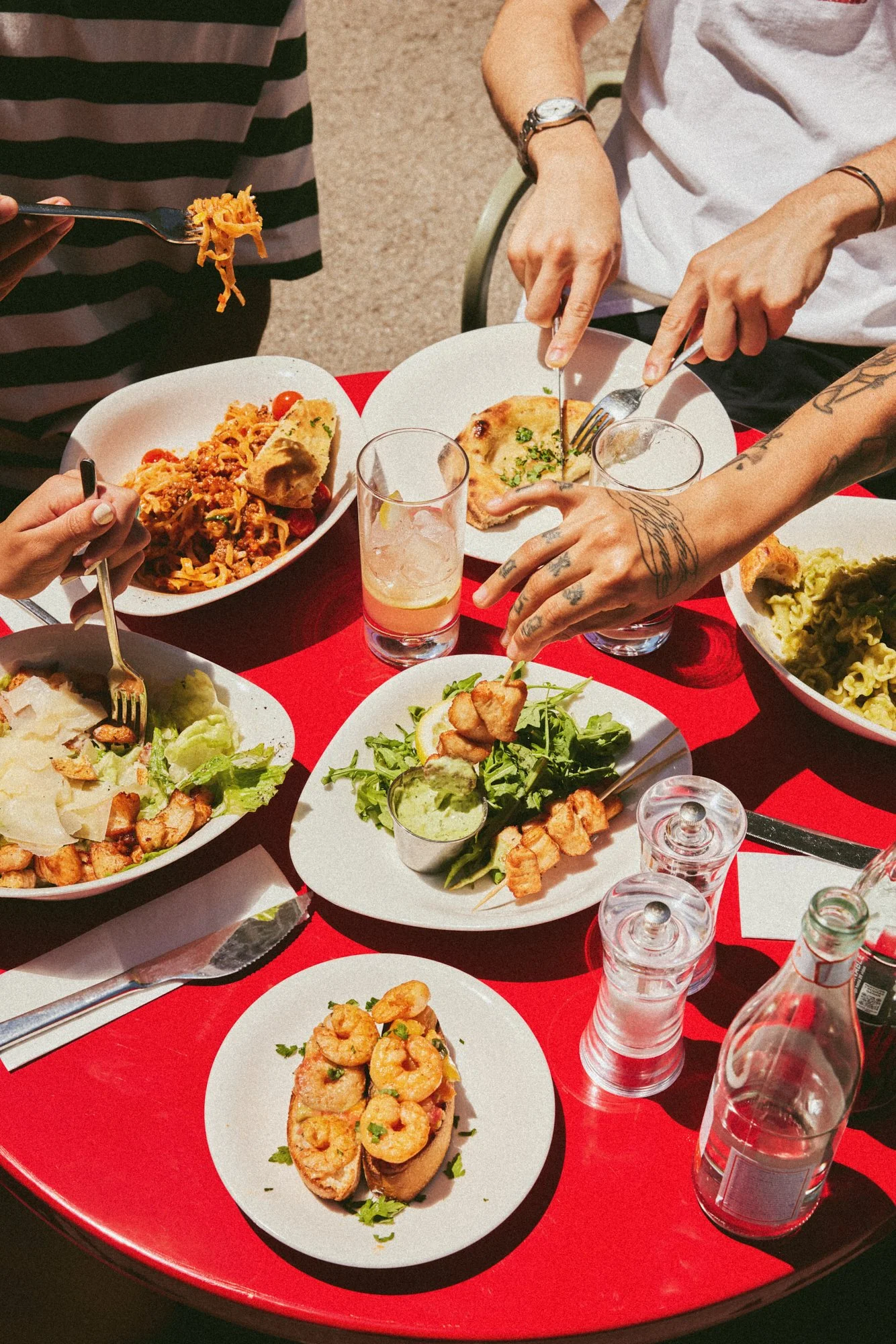 Overhead photograph of diners sharing Italian dishes around a red restaurant table.