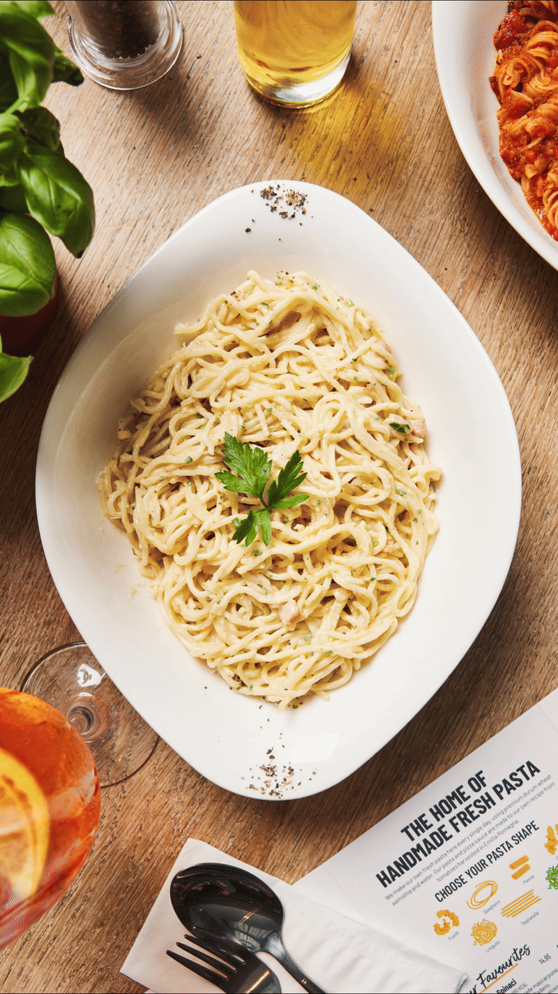 Overhead stop motion GIF of pasta changing on a wooden restaurant table.