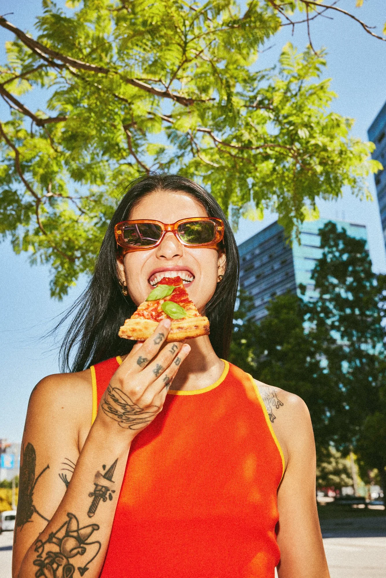 Woman in orange sunglasses eating pizza outdoors in the sunshine.