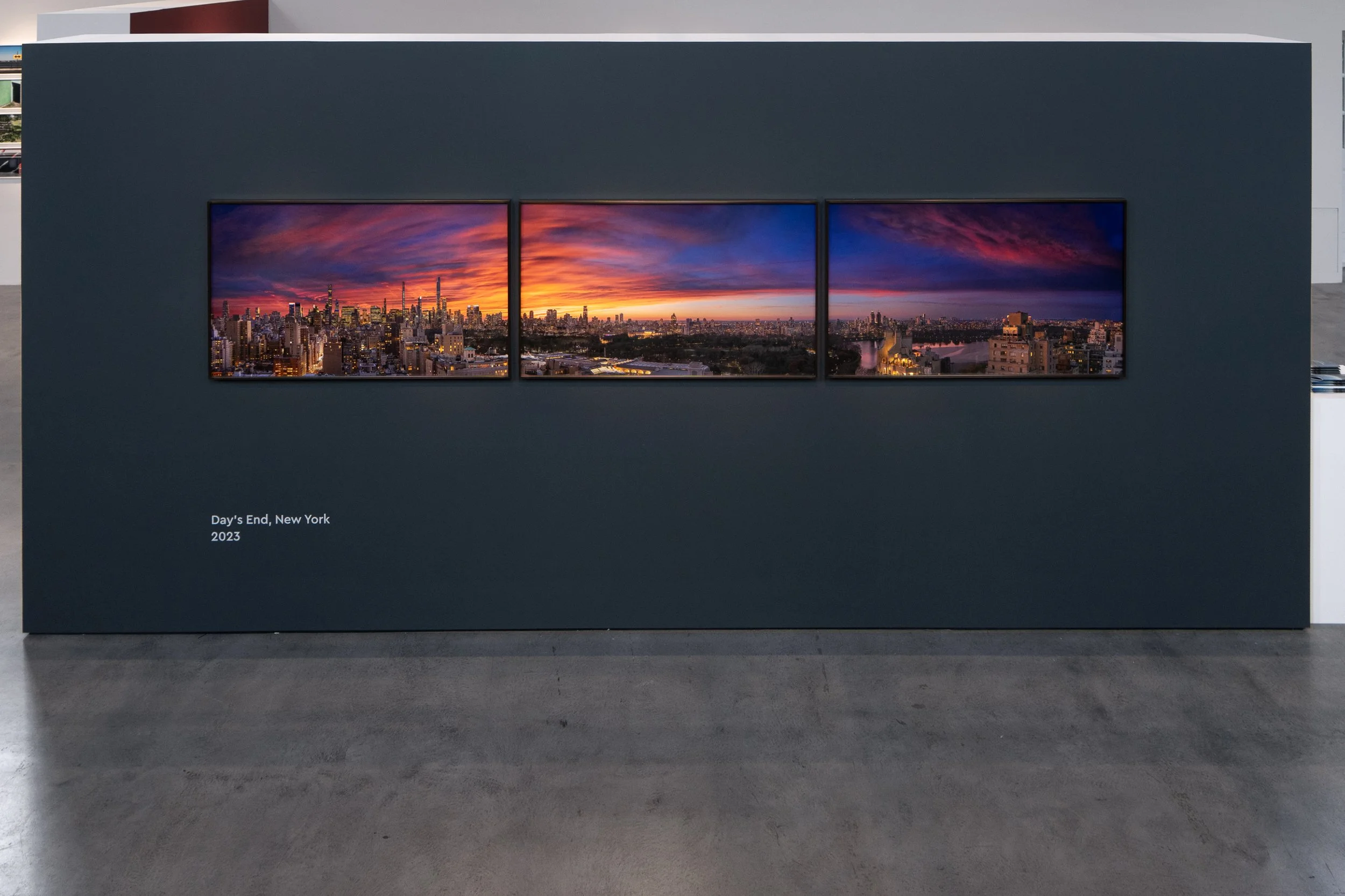 A three-panel photograph of New York City at sunset, mounted on a dark wall, with the caption 'Day's End, New York 2023' in the lower left corner.