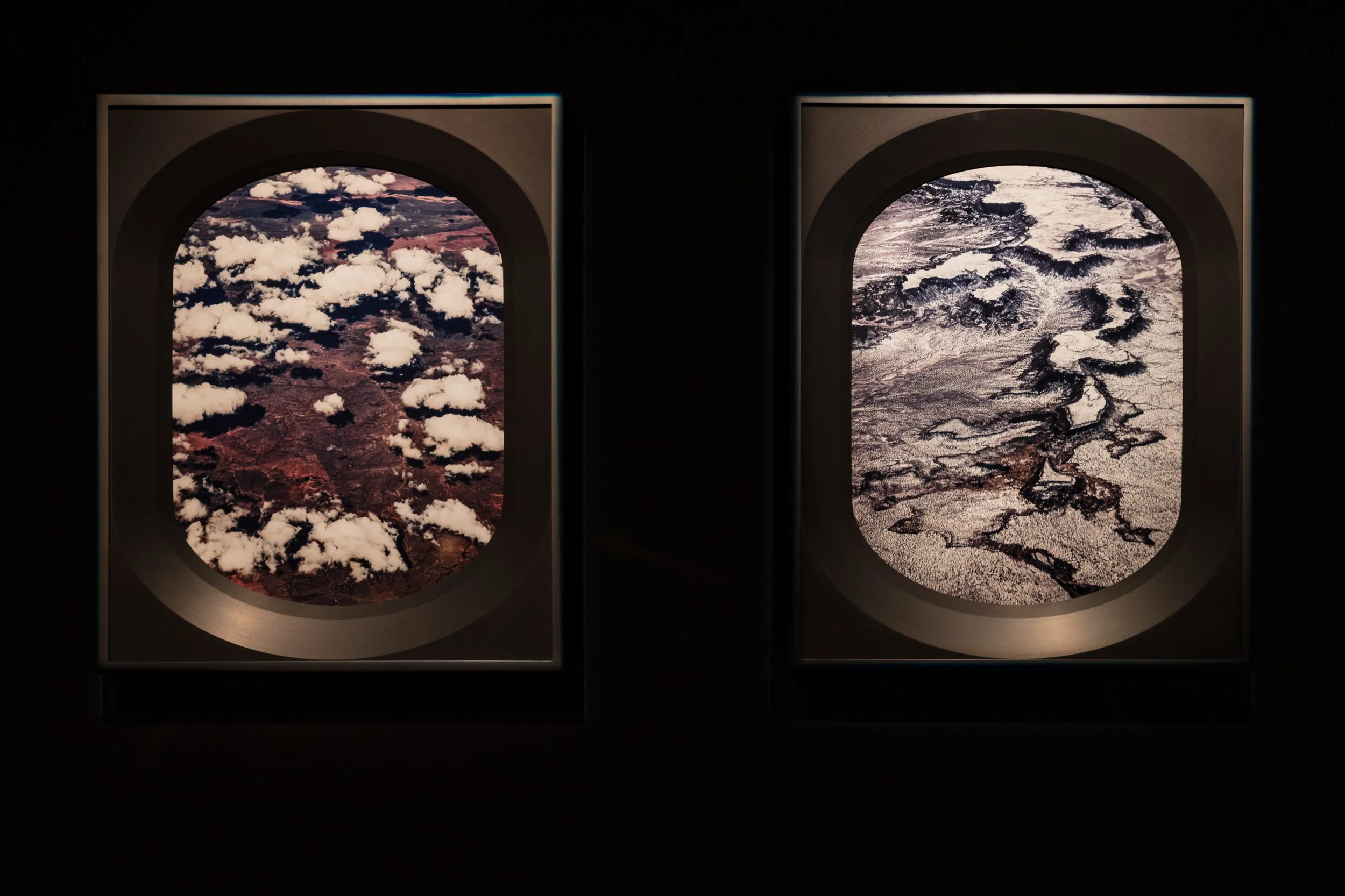 View of Earth's landscapes seen through airplane windows, with one window showing land and clouds and the other showing snow-covered terrain with rivers.