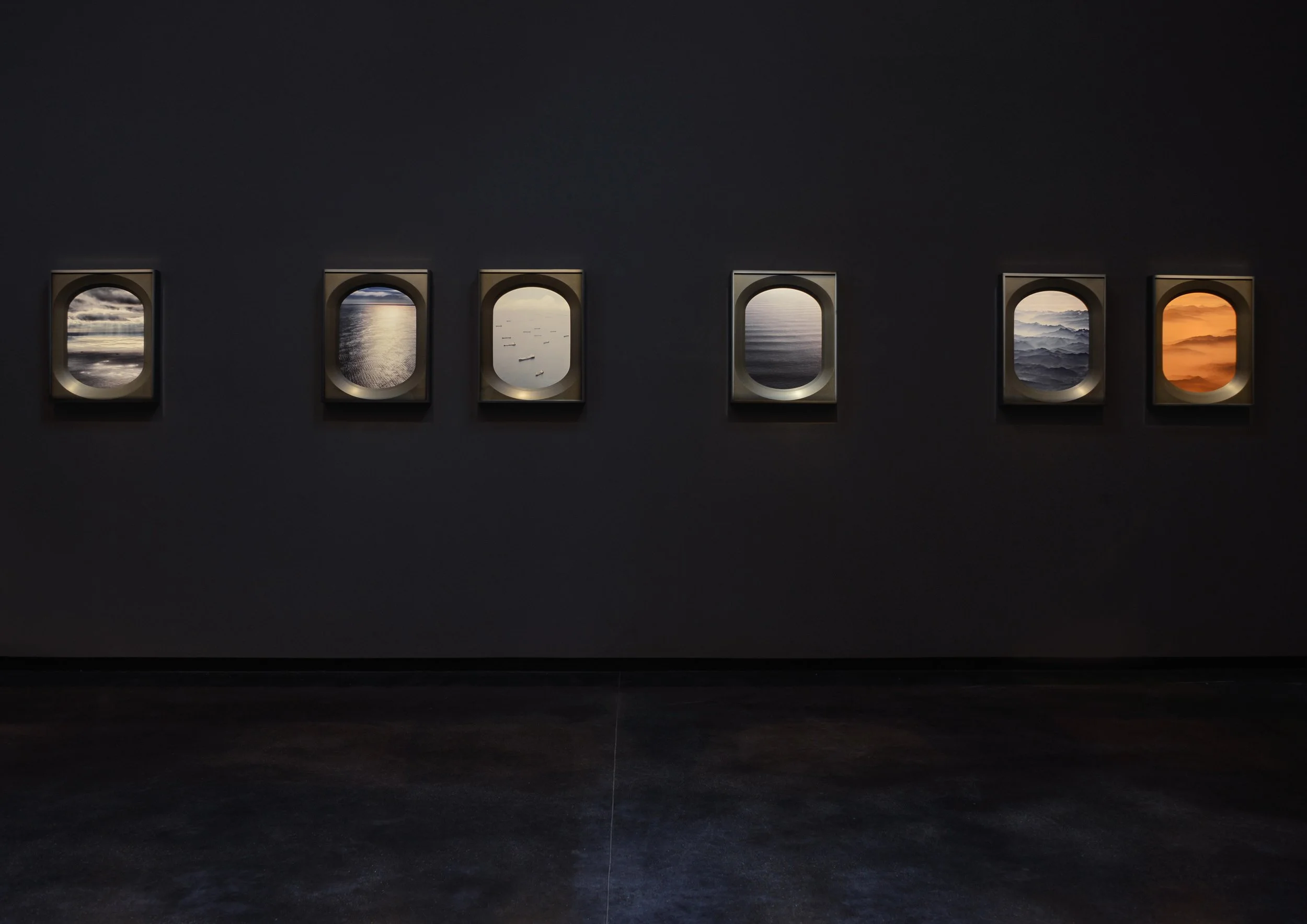 Six framed landscape photographs depicting water scenes, arranged in a row on a dark wall.