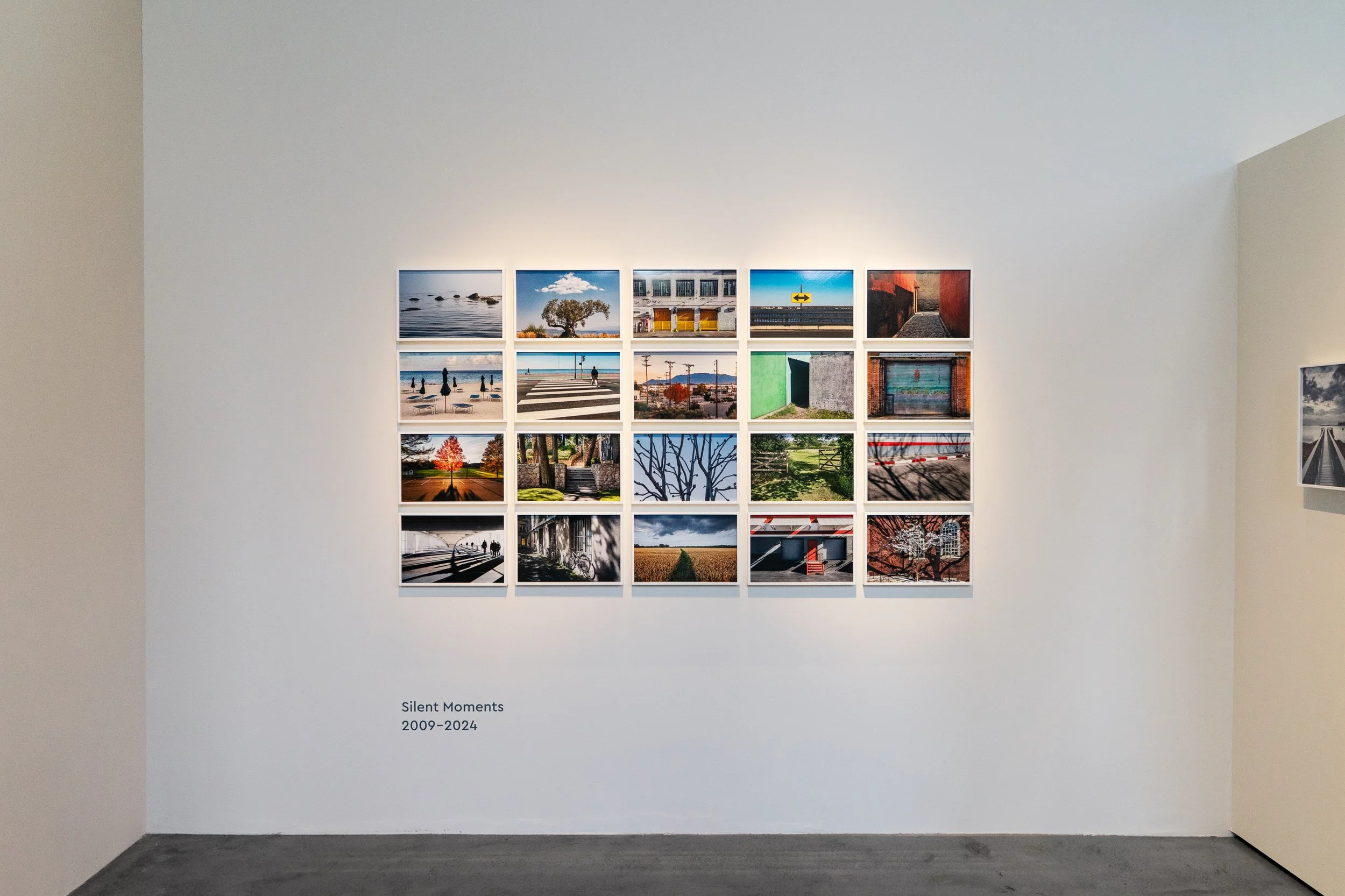 A white gallery wall with a grid of 16 landscape photographs, titled 'Silent Moments 2009-2024'.