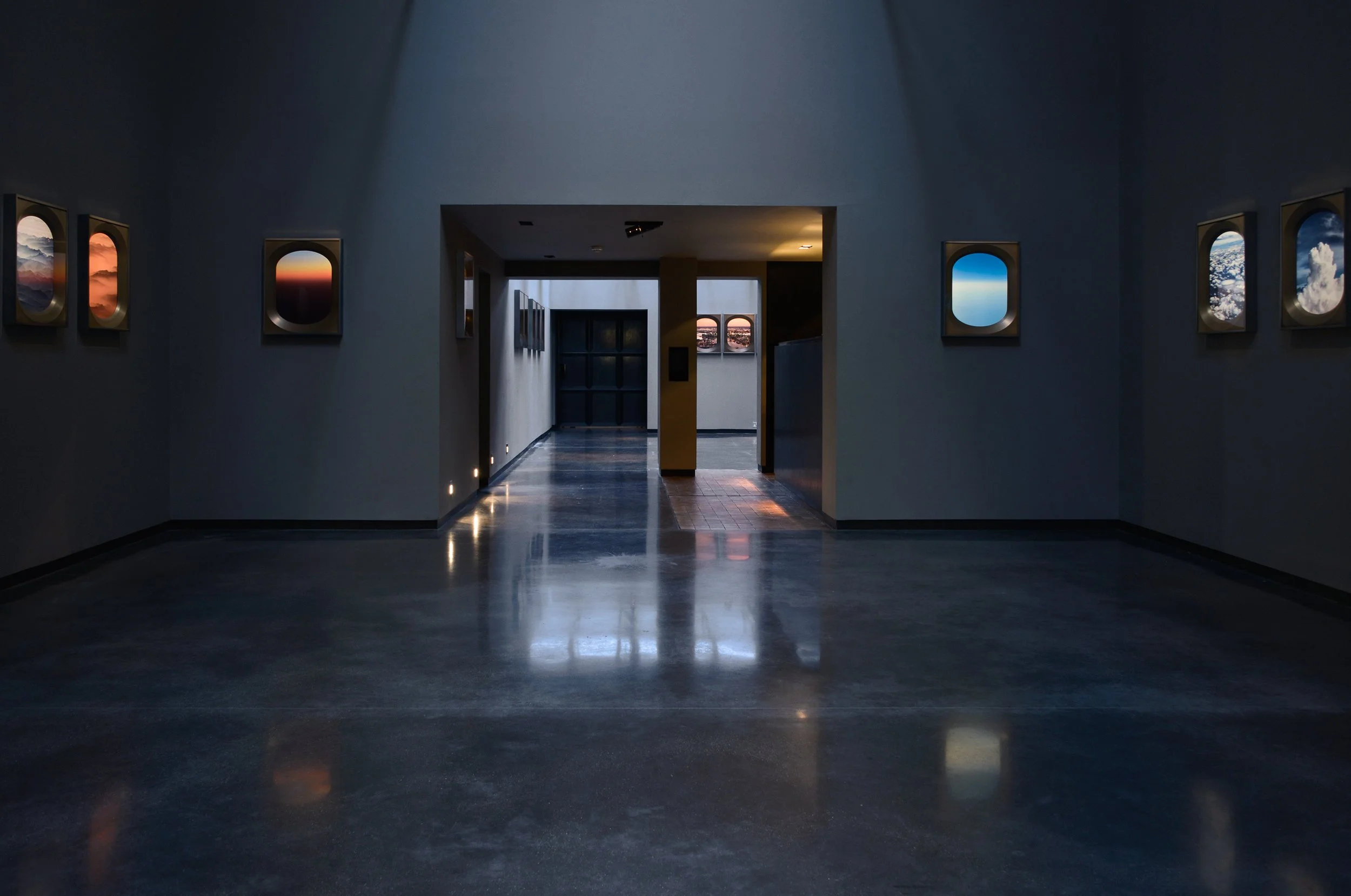 Interior of an art gallery with framed landscape photographs on the walls, dim lighting, and a polished floor reflecting the surroundings.