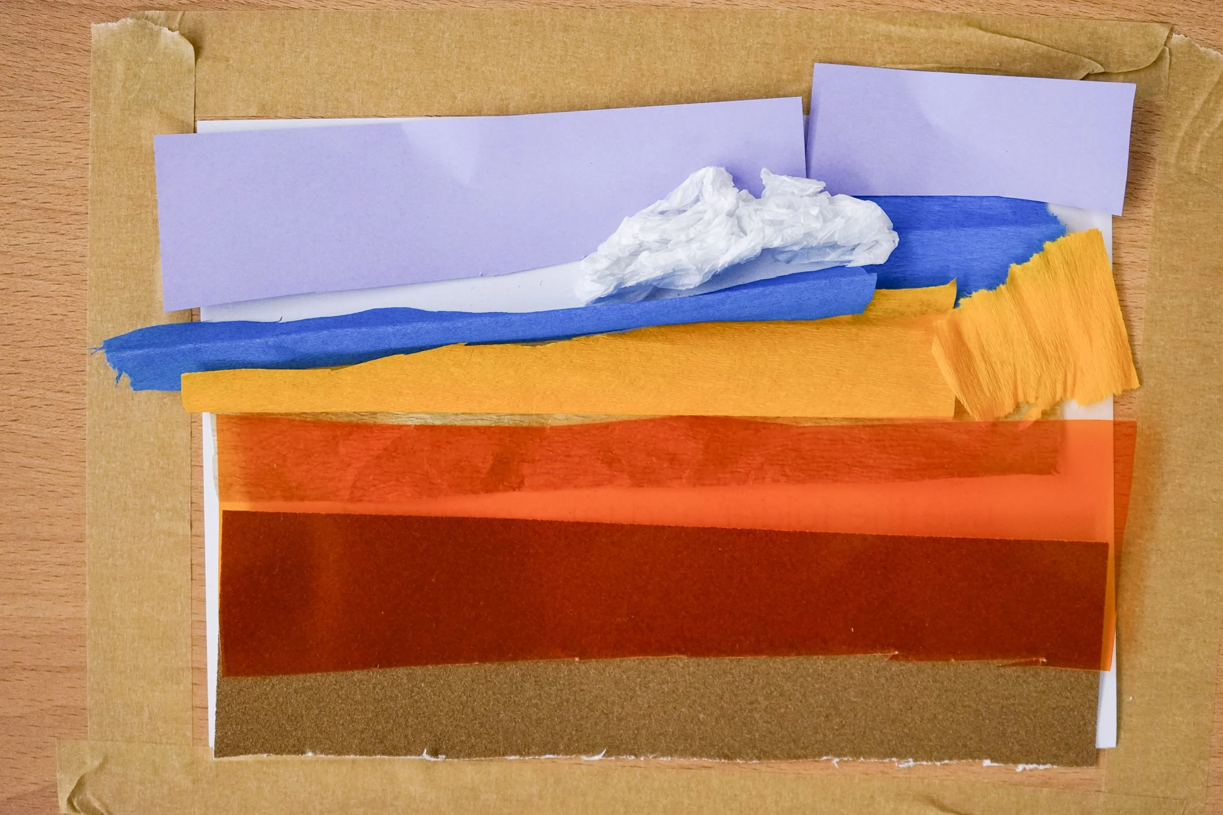 Abstract collage of multiple torn and layered papers in shades of purple, blue, orange, red, and brown, arranged on a wooden surface.