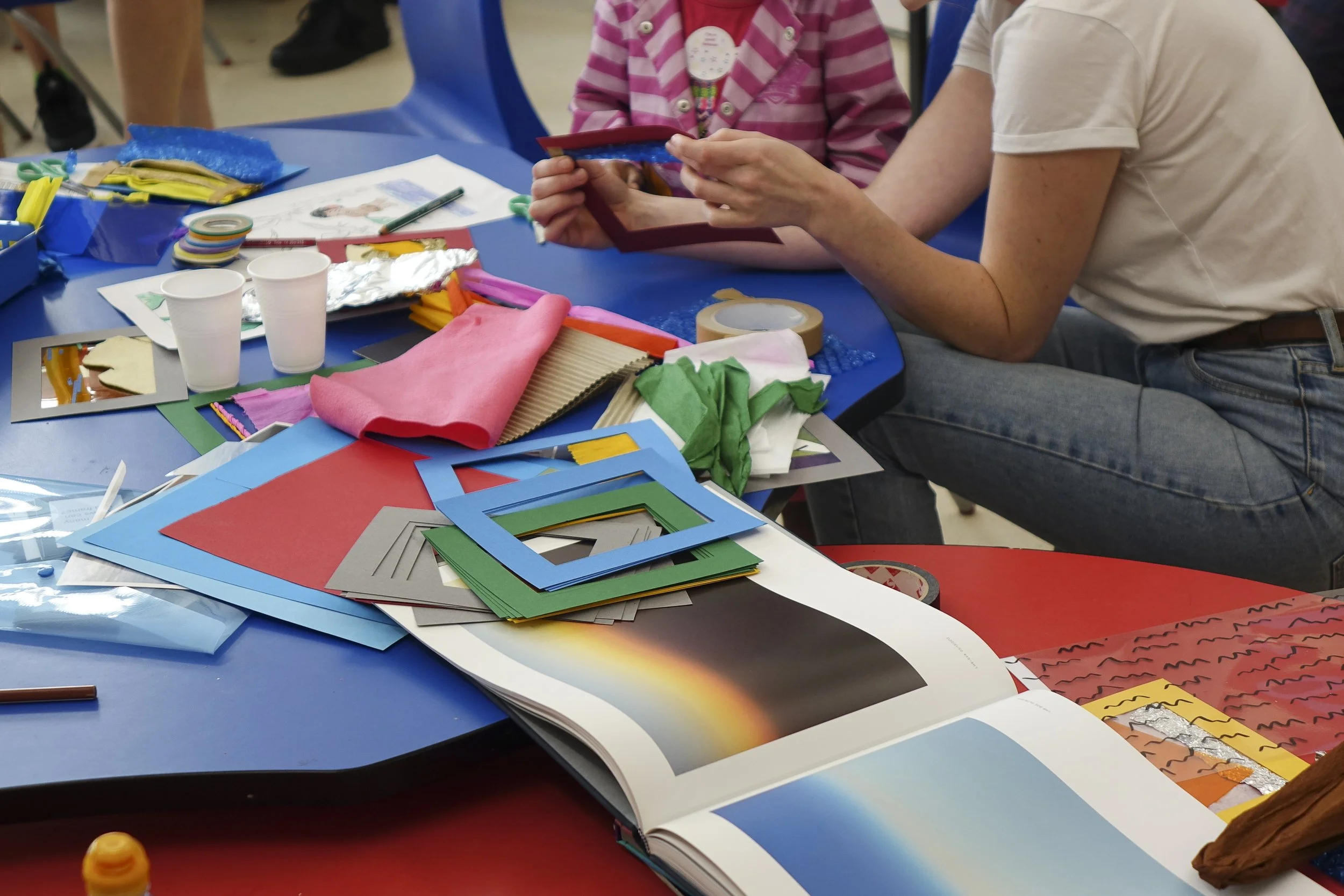 People sitting at a table engaged in arts and crafts, surrounded by construction paper, scissors, tape, and other crafting supplies.
