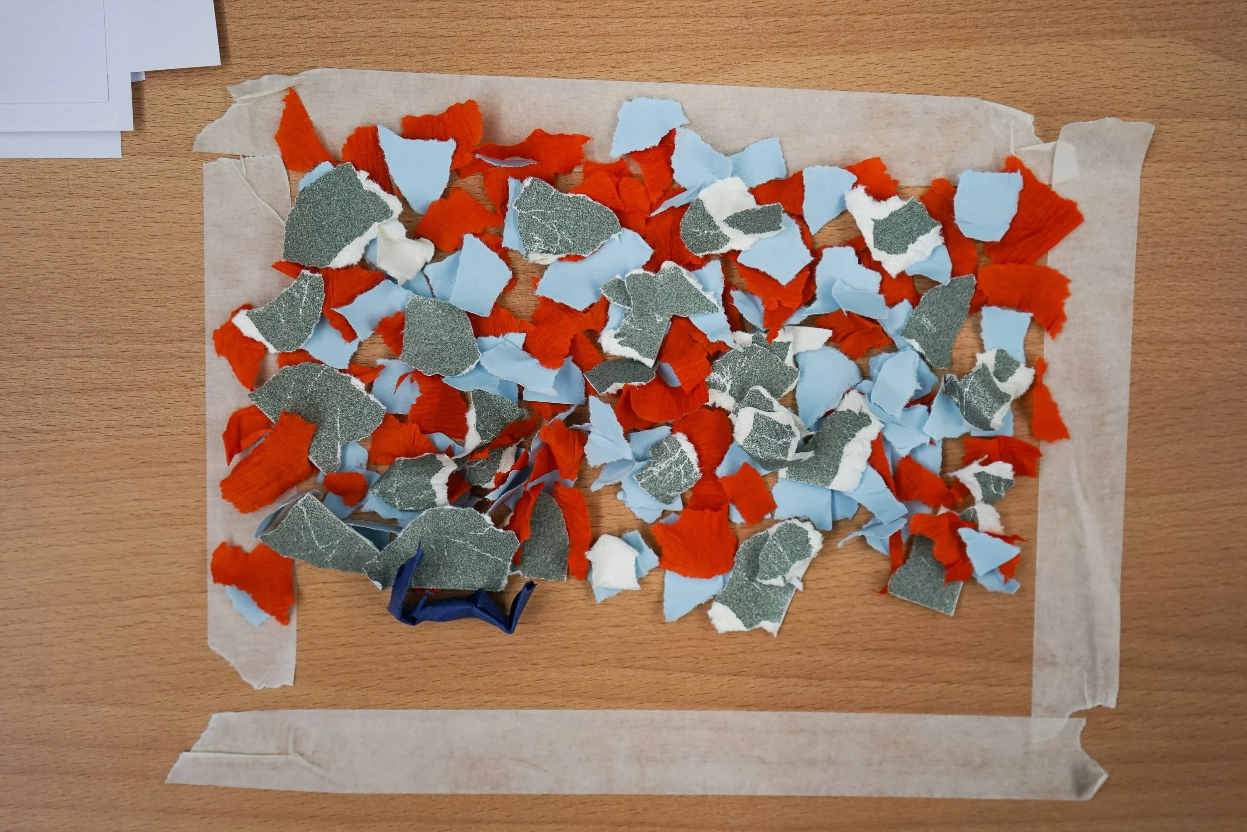 Torn pieces of paper in red, blue, white, and gray colors spread across a piece of parchment paper on a wooden surface.