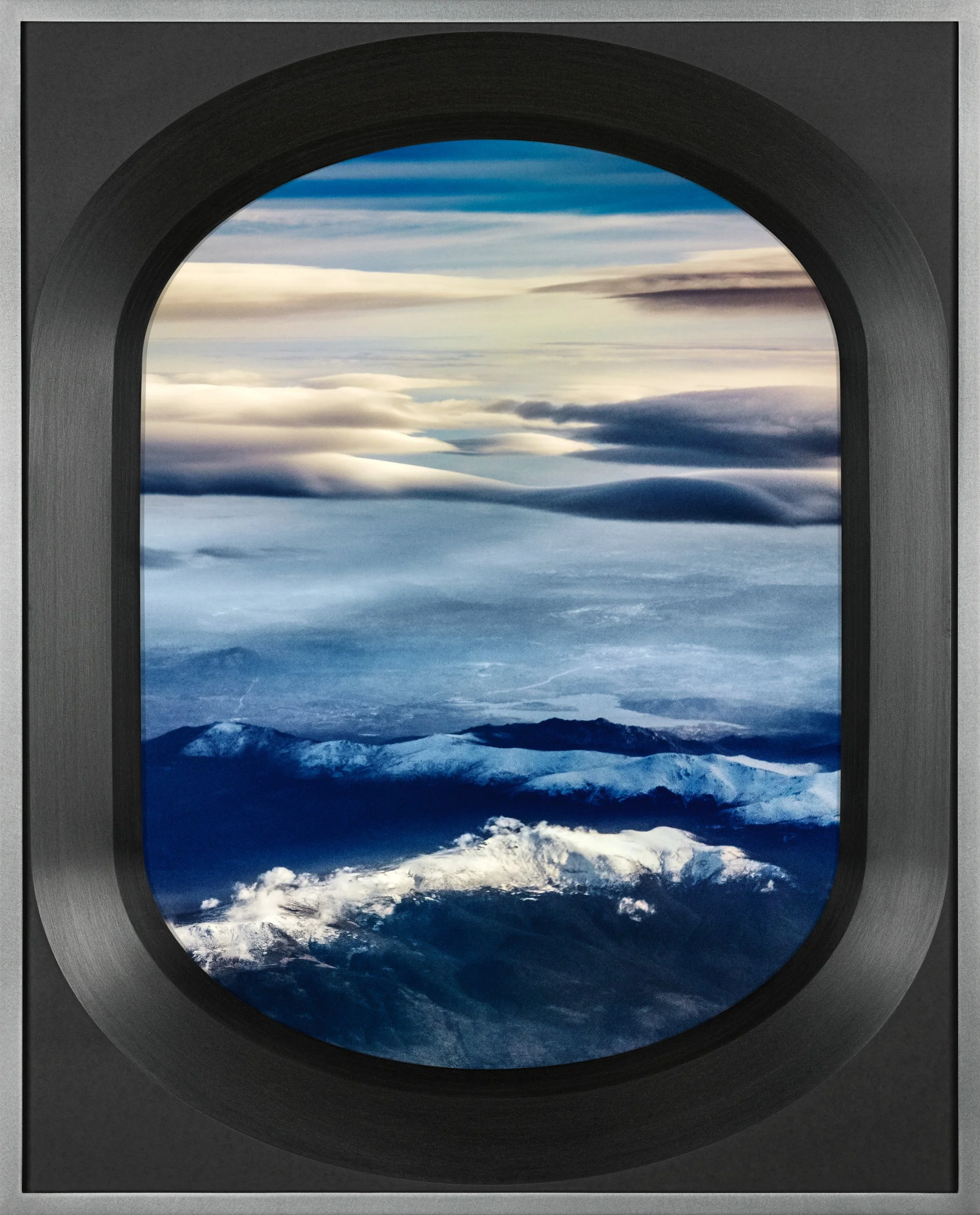 View of earth from space, showing white clouds, blue oceans, snowy mountain peaks, and atmospheric layers through an oval window with a black frame.